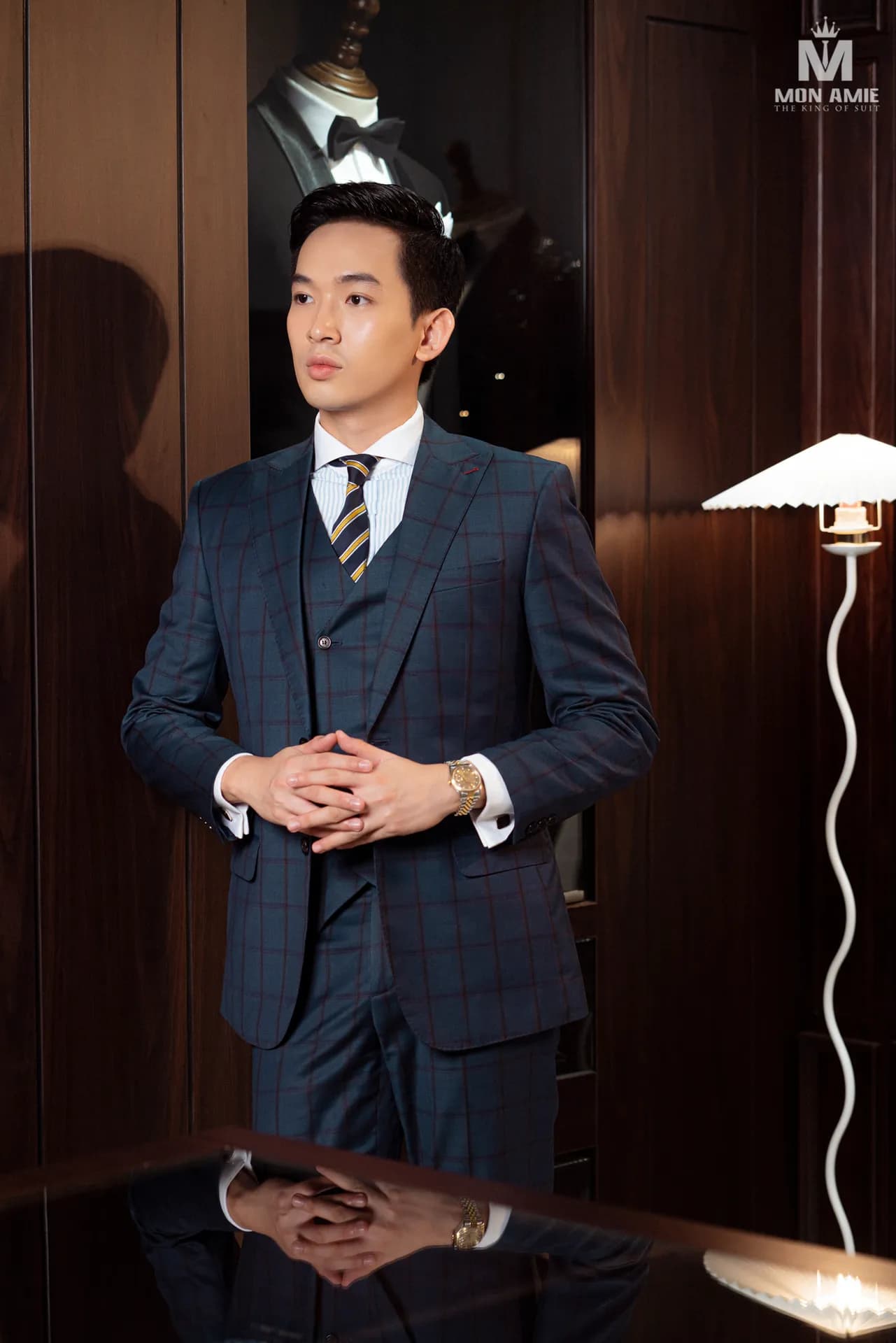 Suit navy kẻ ô ba mảnh, chắp tay đứng bên đèn sàn trong showroom