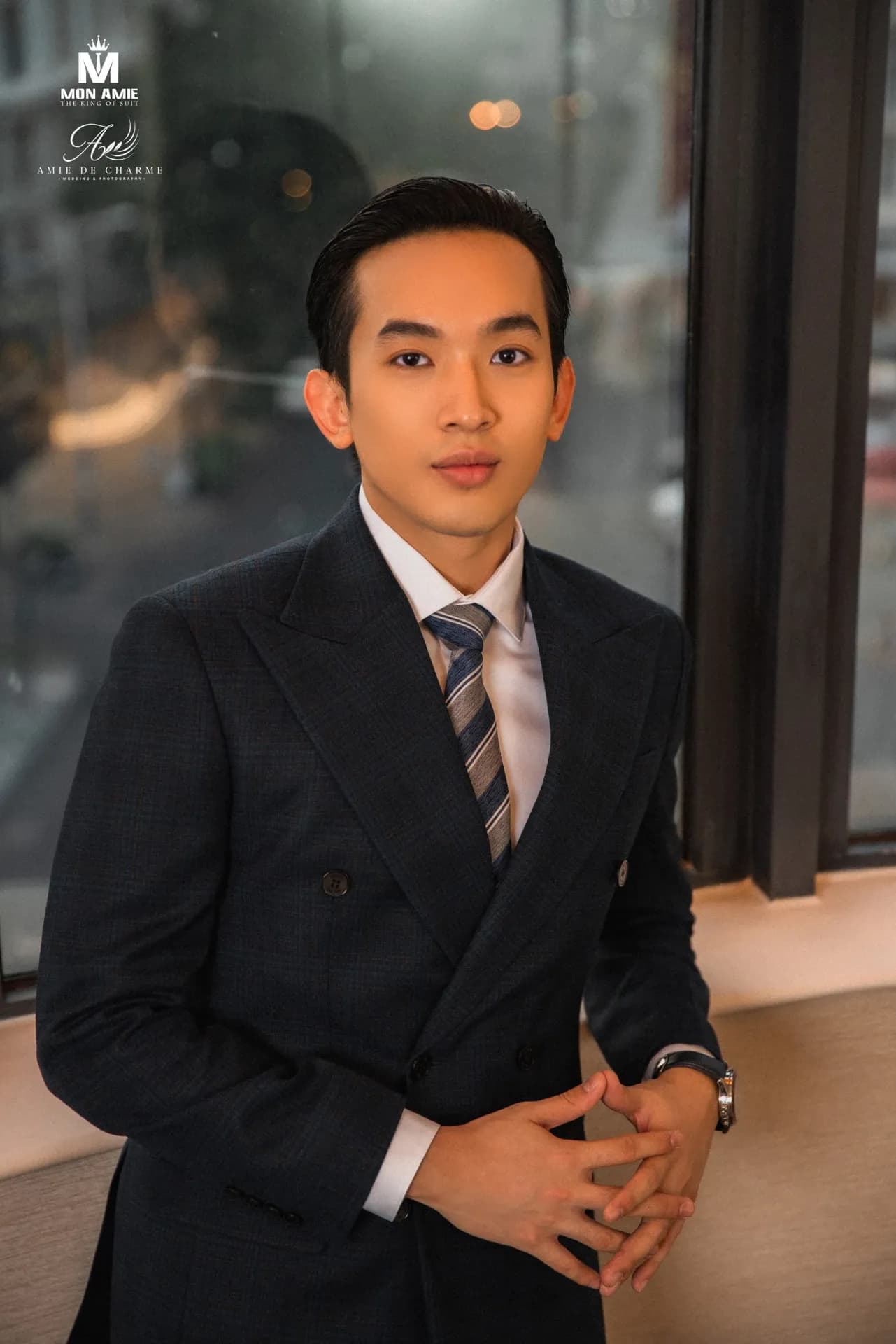 Suit navy cài hai hàng, hai tay đan nhau bên cửa sổ, ánh sáng ấm hoàng hôn