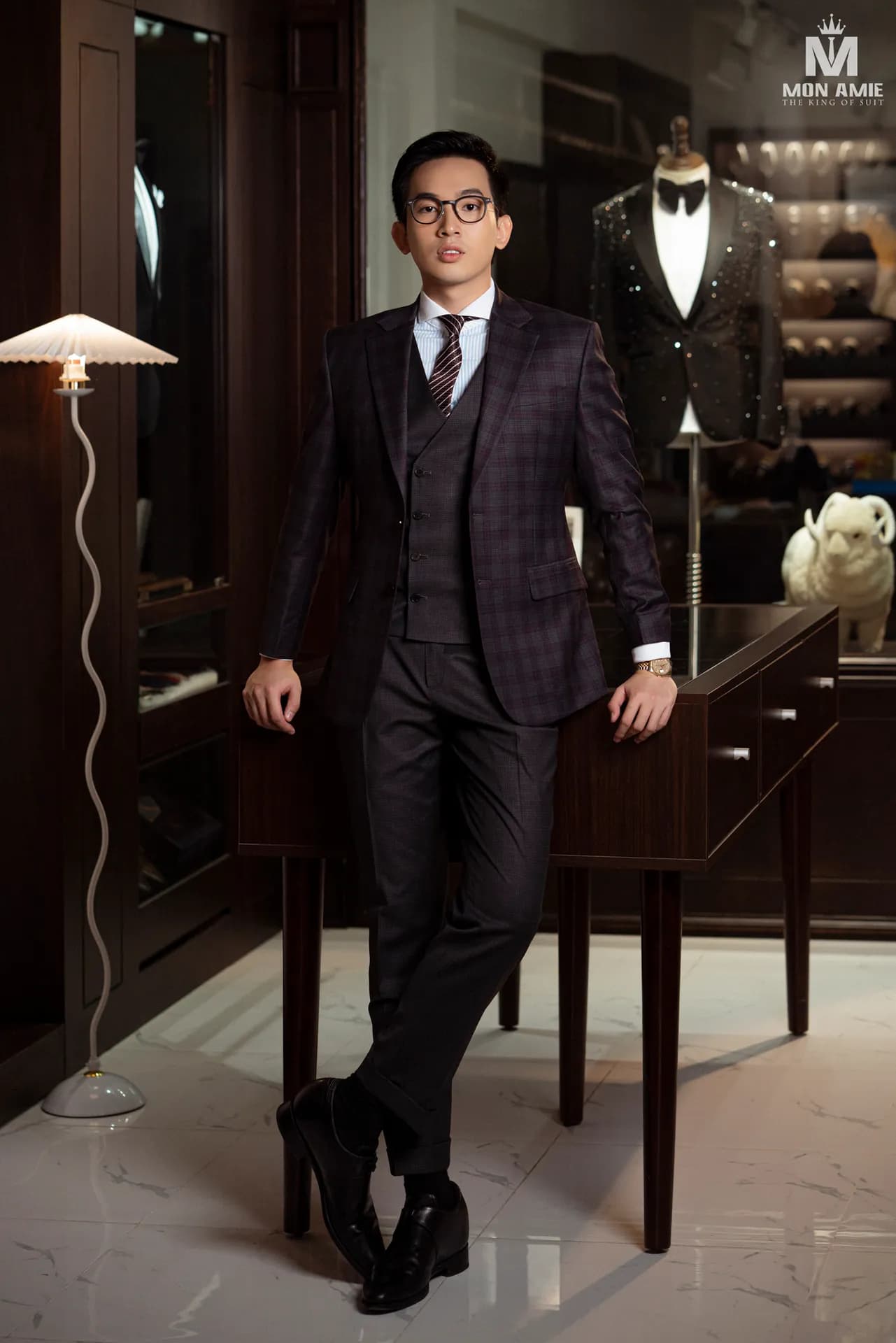 Suit ba mảnh kẻ ô tựa bàn gỗ, toàn thân trong showroom