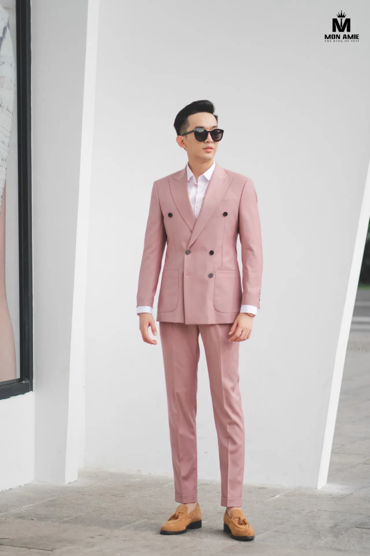 Suit hồng phấn hai hàng khuy, kính râm, đứng toàn thân trước bức tường trắng