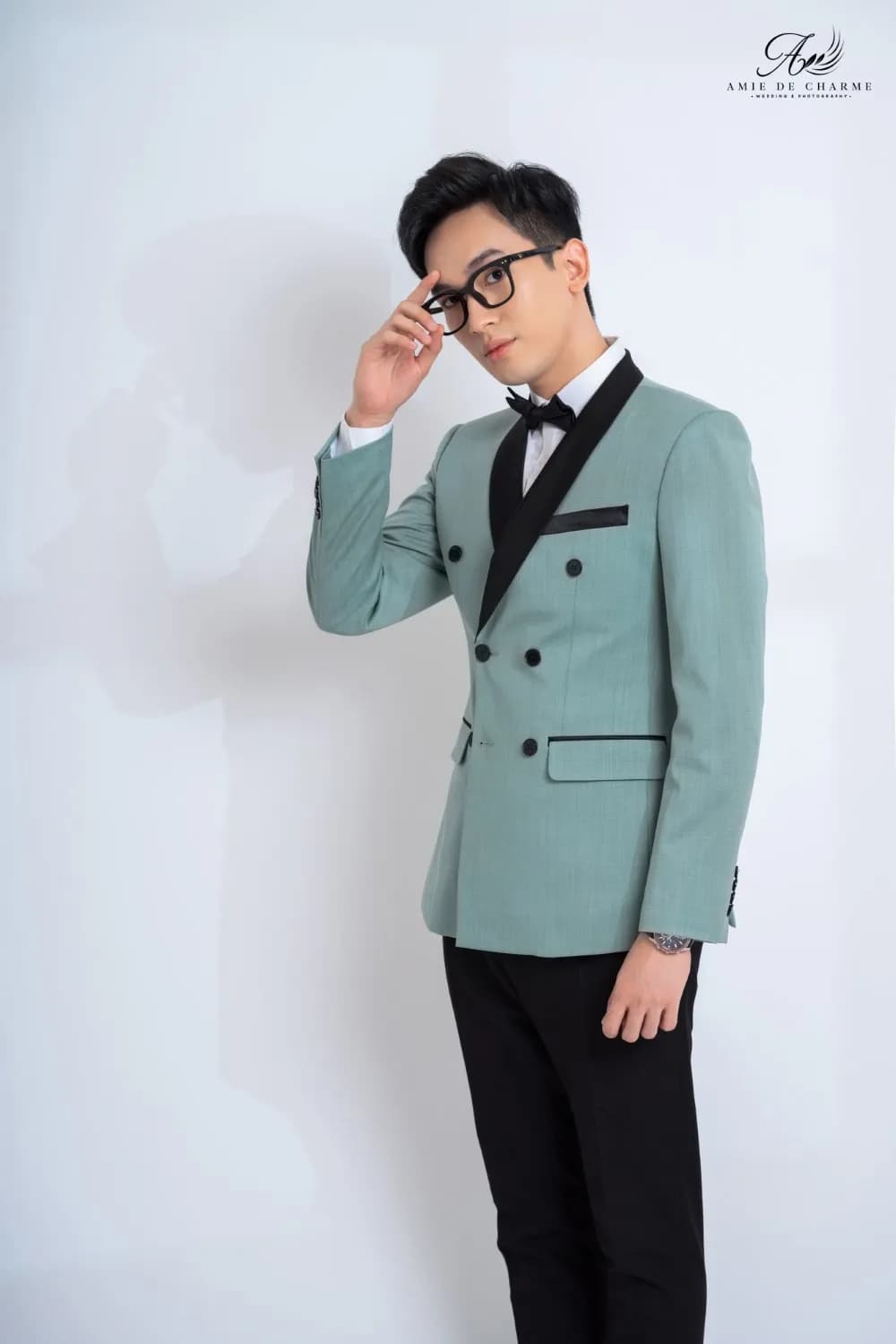 Blazer xanh bạc hà cài hai hàng cổ ve satin đen, tay chạm gọng kính