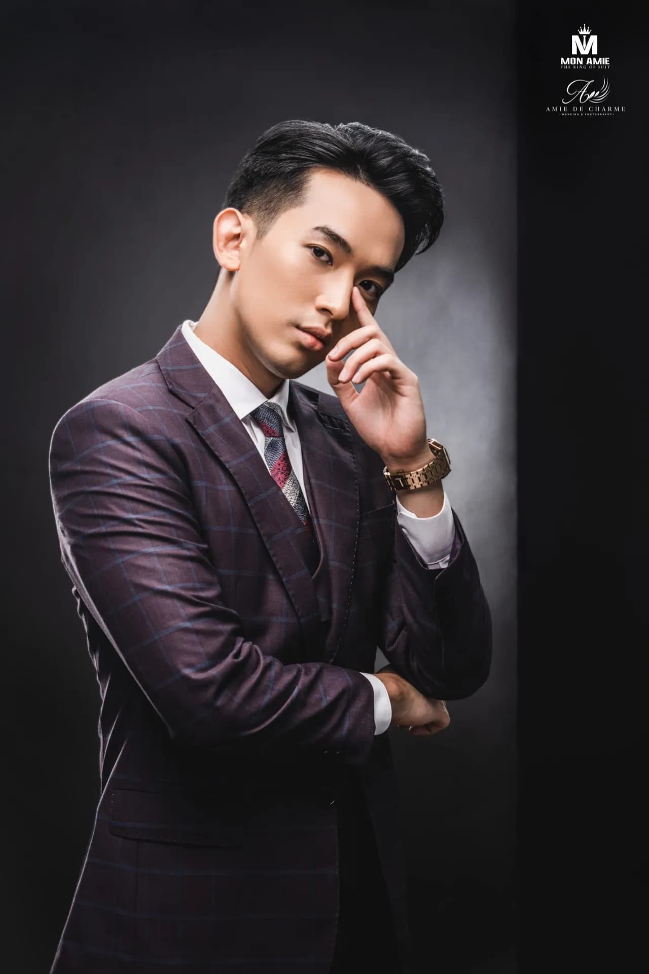 Suit ba mảnh tím than kẻ ô, tay chạm má, ánh nhìn trầm, chân dung nền tối