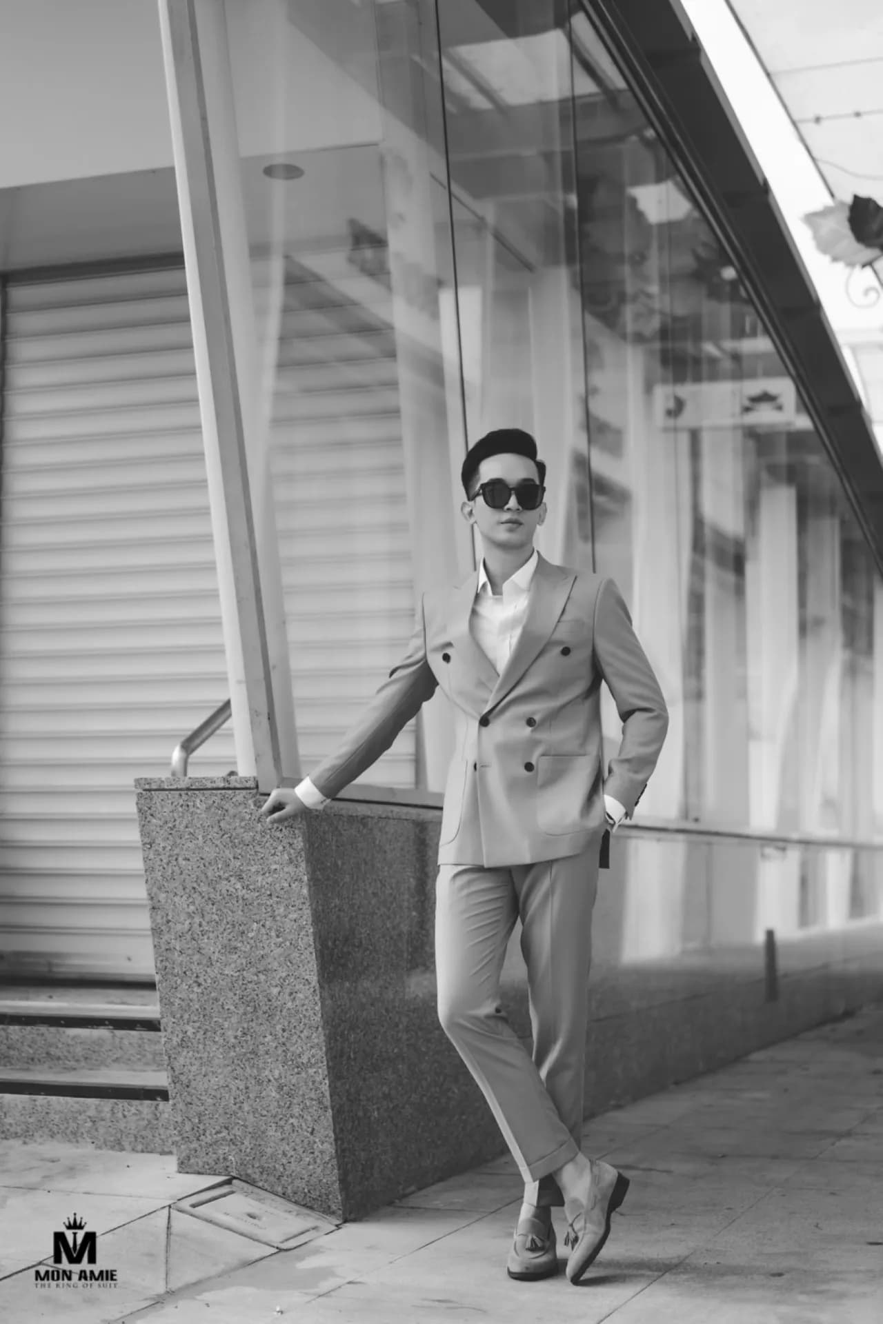 Suit hai hàng khuy xám, kính râm, ảnh đen trắng tựa tường đá
