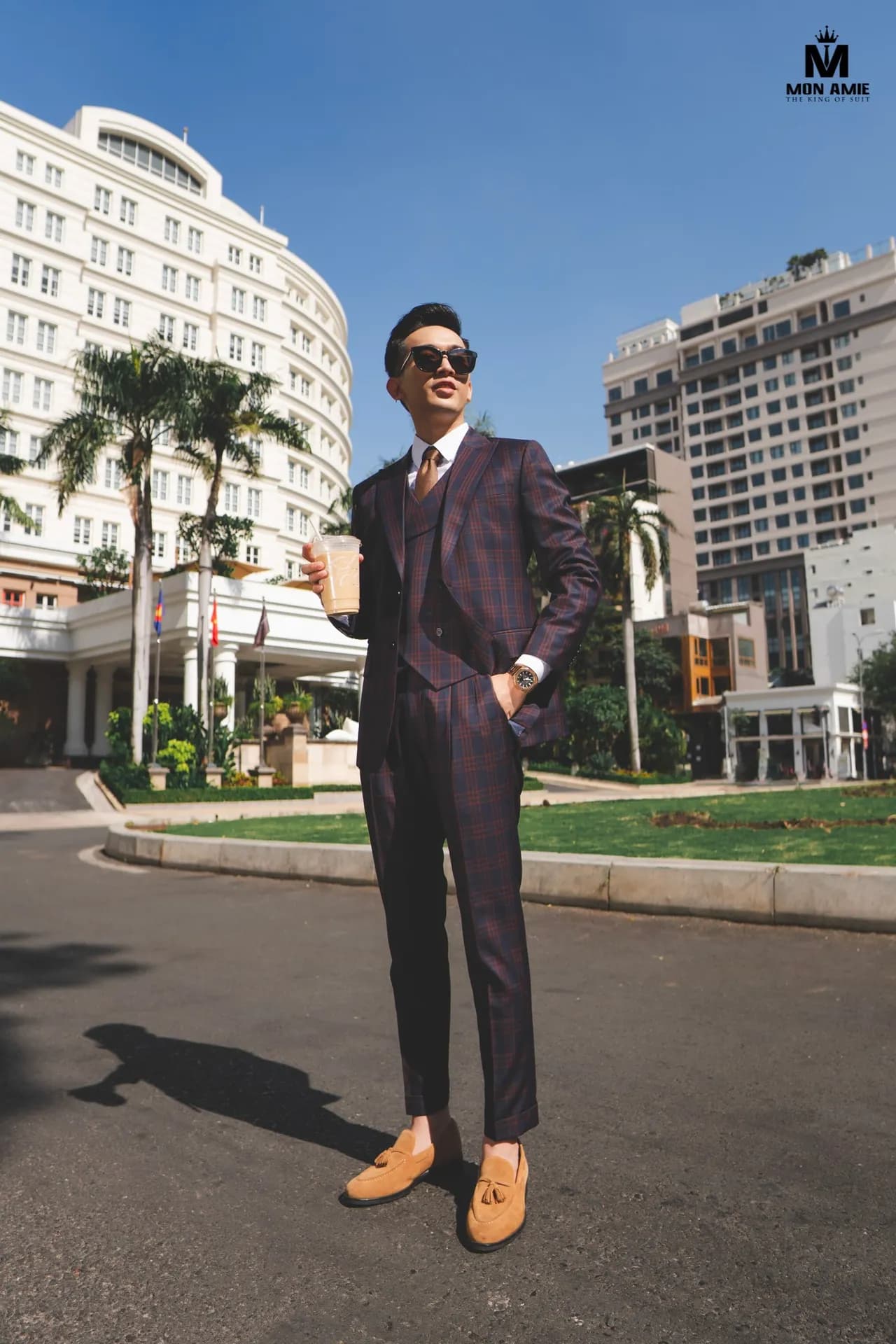 Suit ba mảnh caro tím, sải bước giữa đường, nền cọ và khách sạn