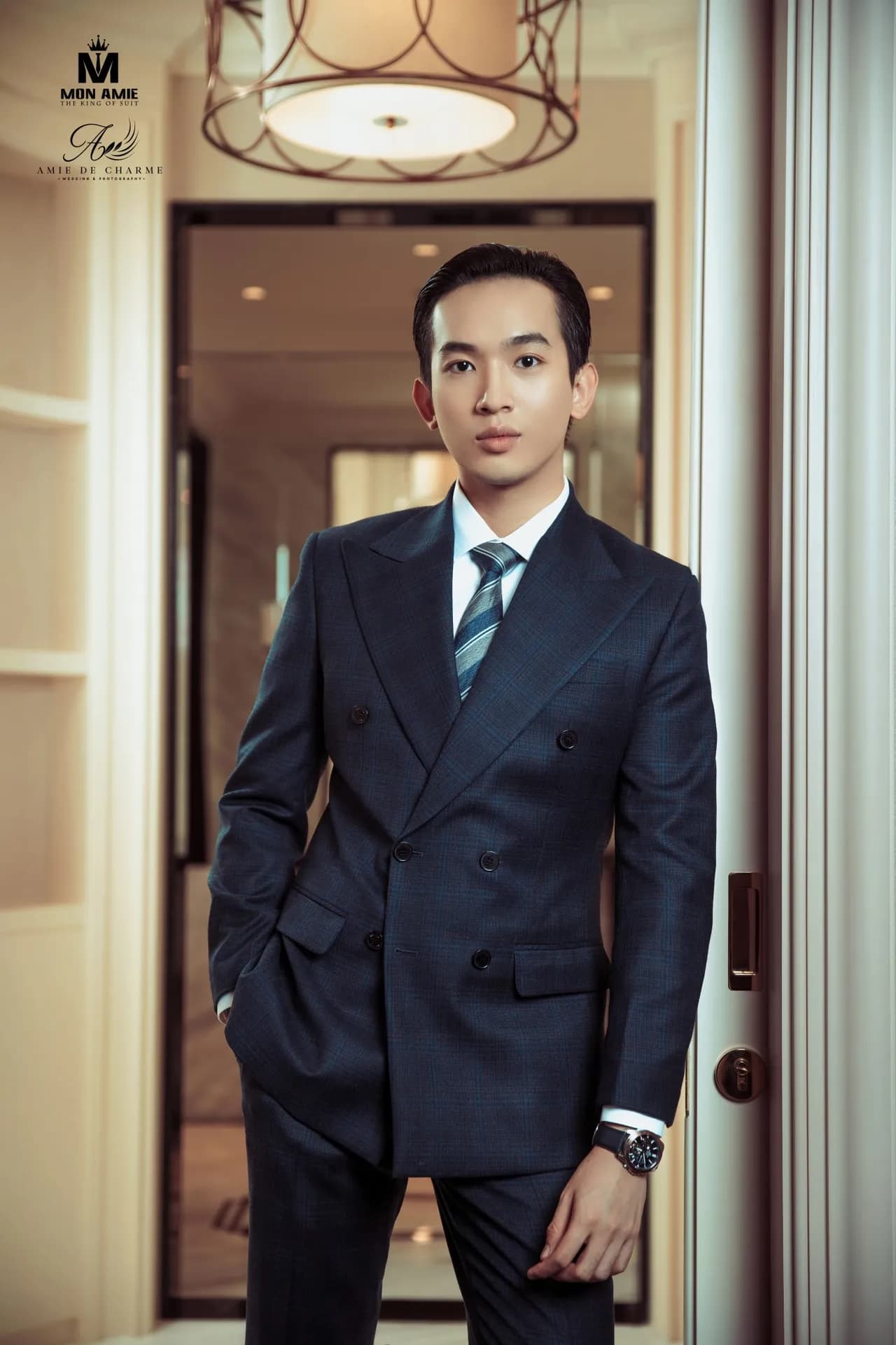 Suit navy cài hai hàng, cà vạt sọc, tay đút túi, ánh nhìn tự tin trong sảnh
