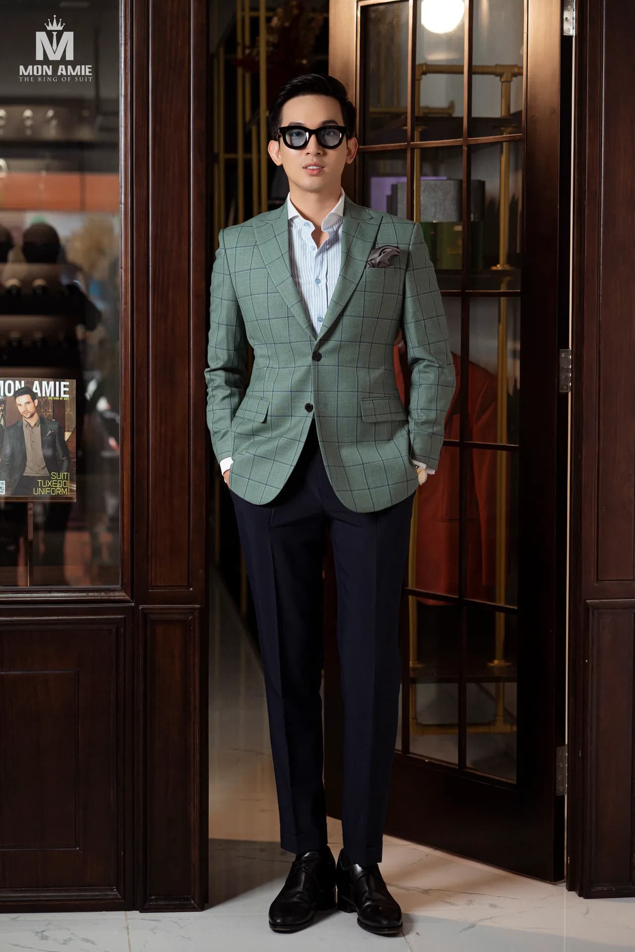 Blazer xanh sage phối quần navy, kính râm, đứng trước tủ gỗ