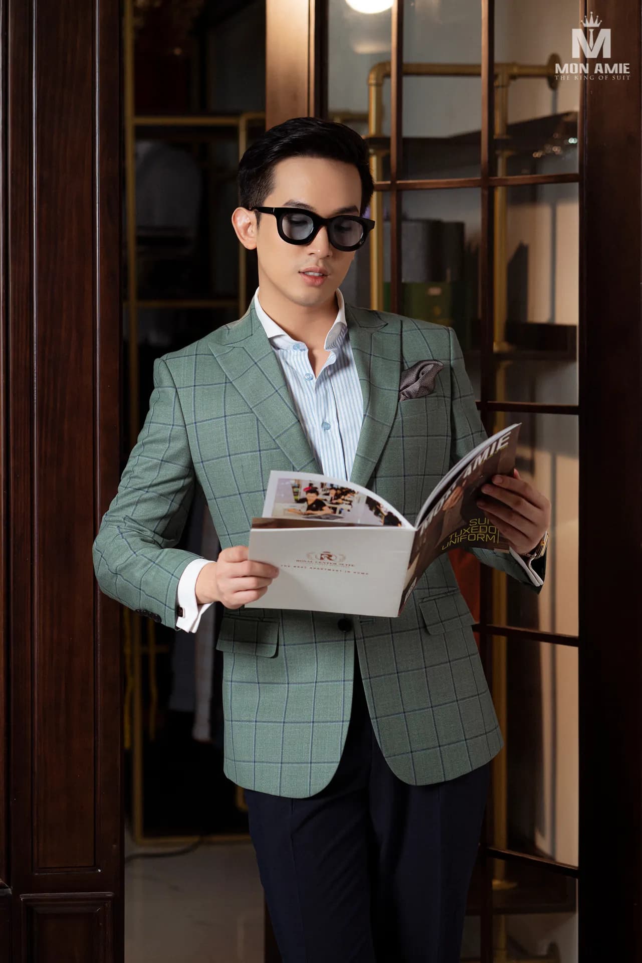 Blazer xanh sage kẻ ô, kính râm, đang xem cuốn catalogue