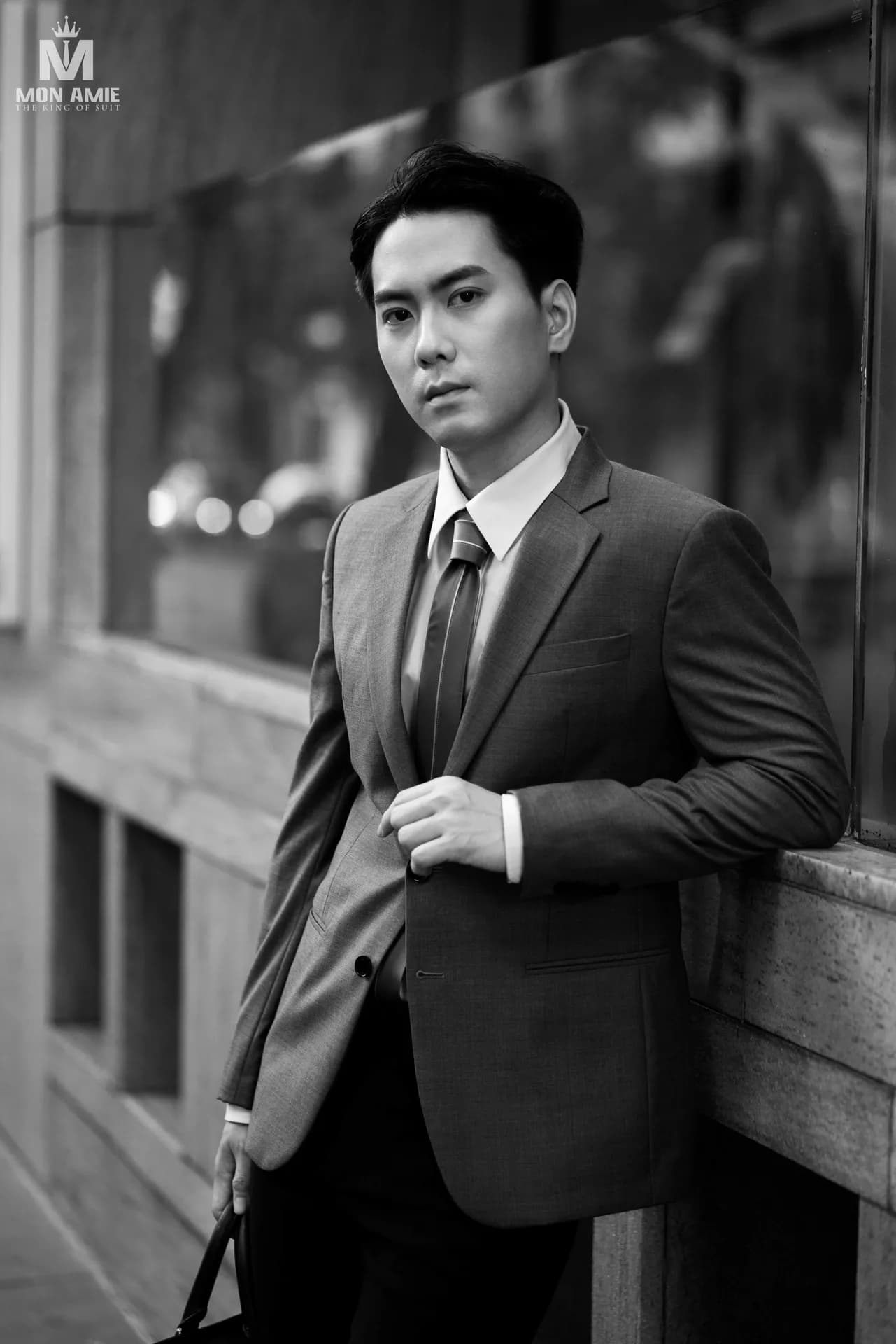 Ảnh đen trắng, tựa tường kính, tay cài khuy áo vest