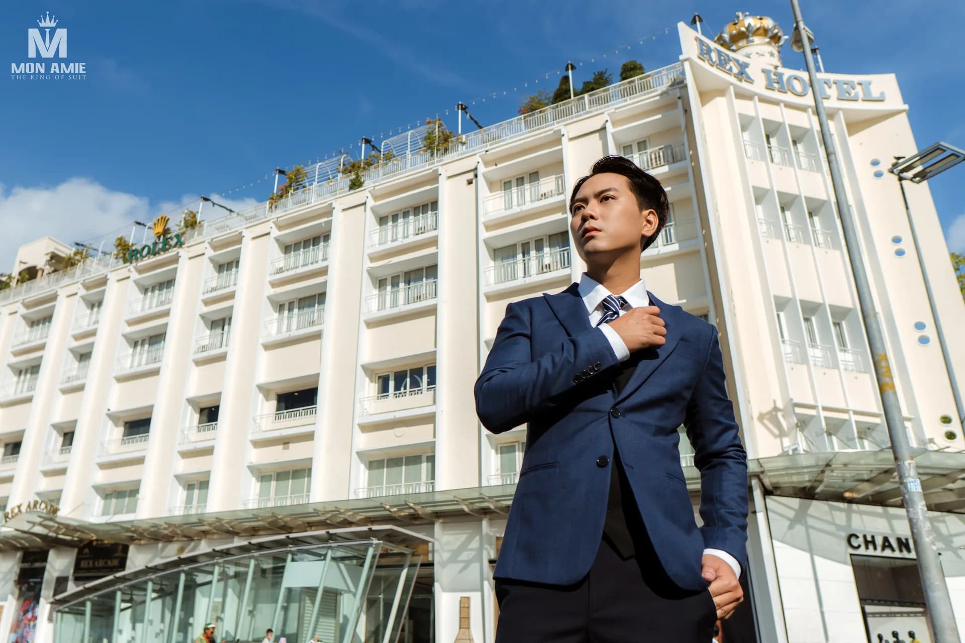 Suit xanh navy trước toà nhà khách sạn lịch sử, khung ngang góc thấp
