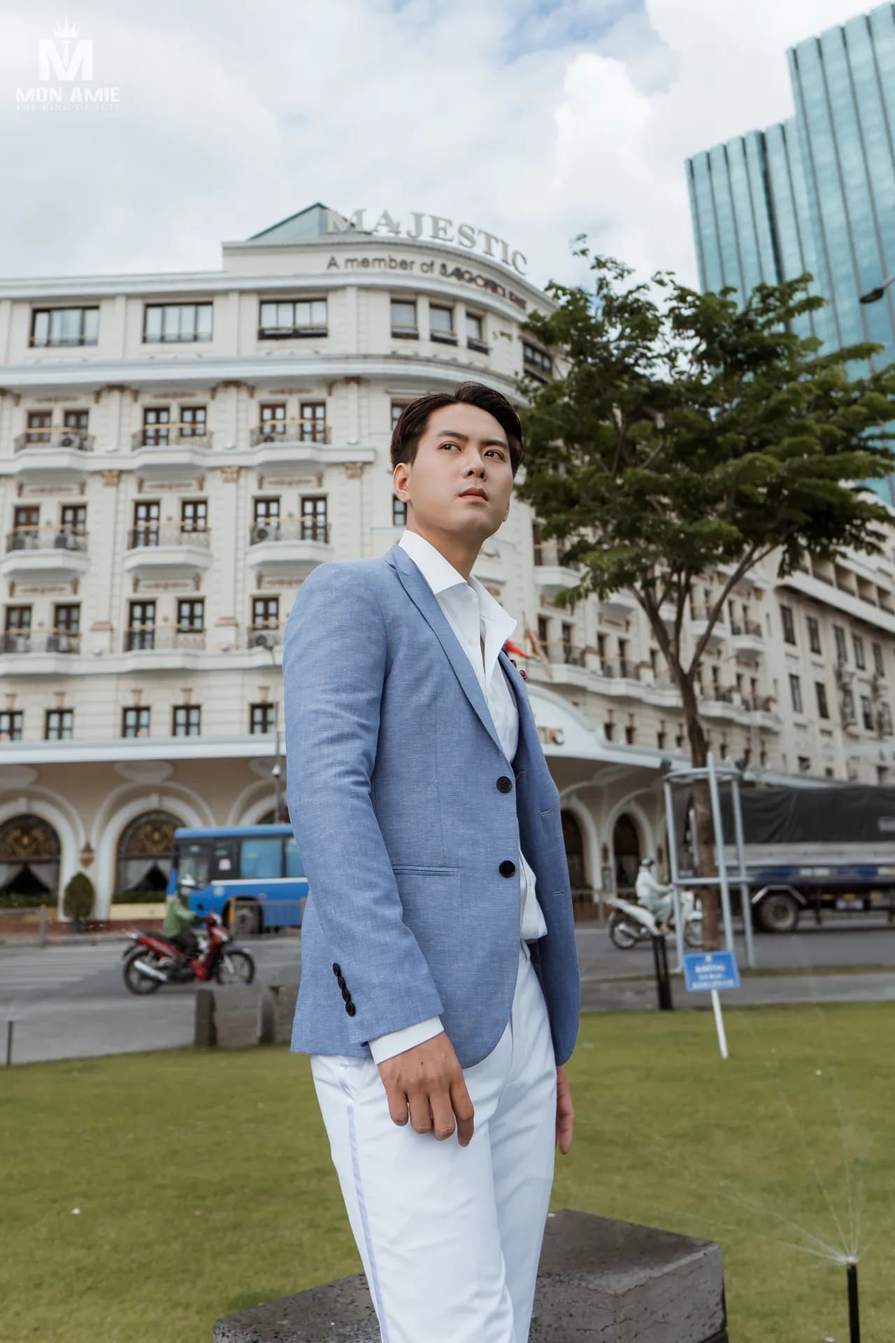 Vest xanh linen nhạt, quần trắng, đứng trên bãi cỏ trước khách sạn cổ