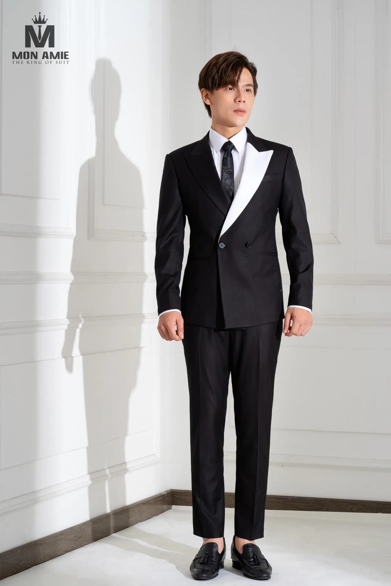 Suit đen hai hàng khuy, ve nhọn phối trắng tương phản, cà vạt hoạ tiết.