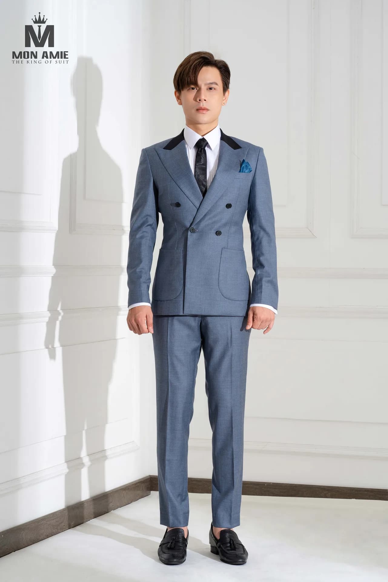 Suit hai hàng khuy xanh xám, ve phối nhung đen tạo điểm nhấn tương phản.