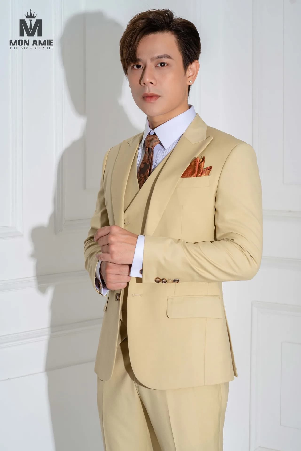 Suit vàng kem ba mảnh, ve nhọn, khăn cài túi cam, dáng bán thân.