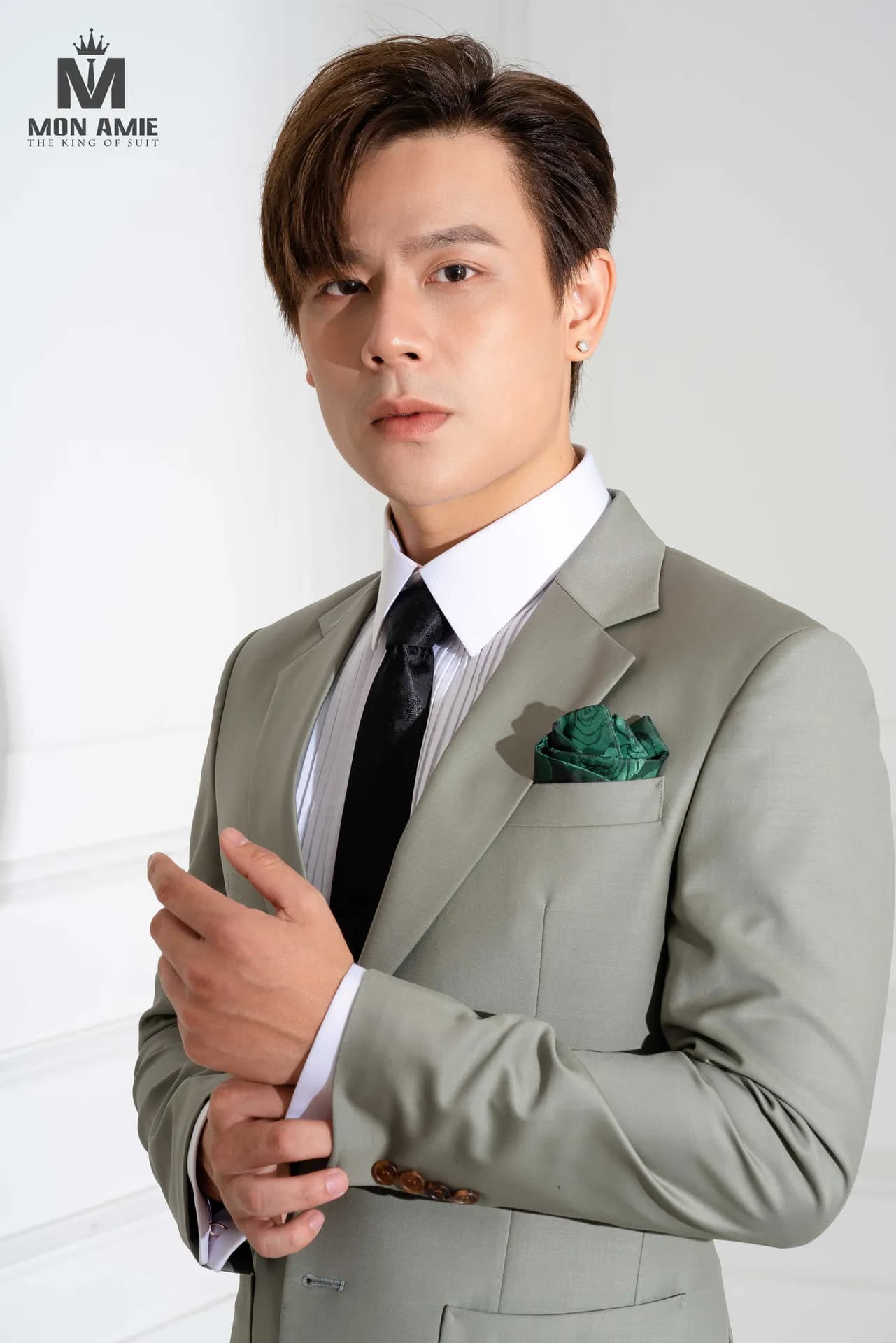 Suit xám xanh, cà vạt đen, khăn cài túi xanh lá, chỉnh măng sét