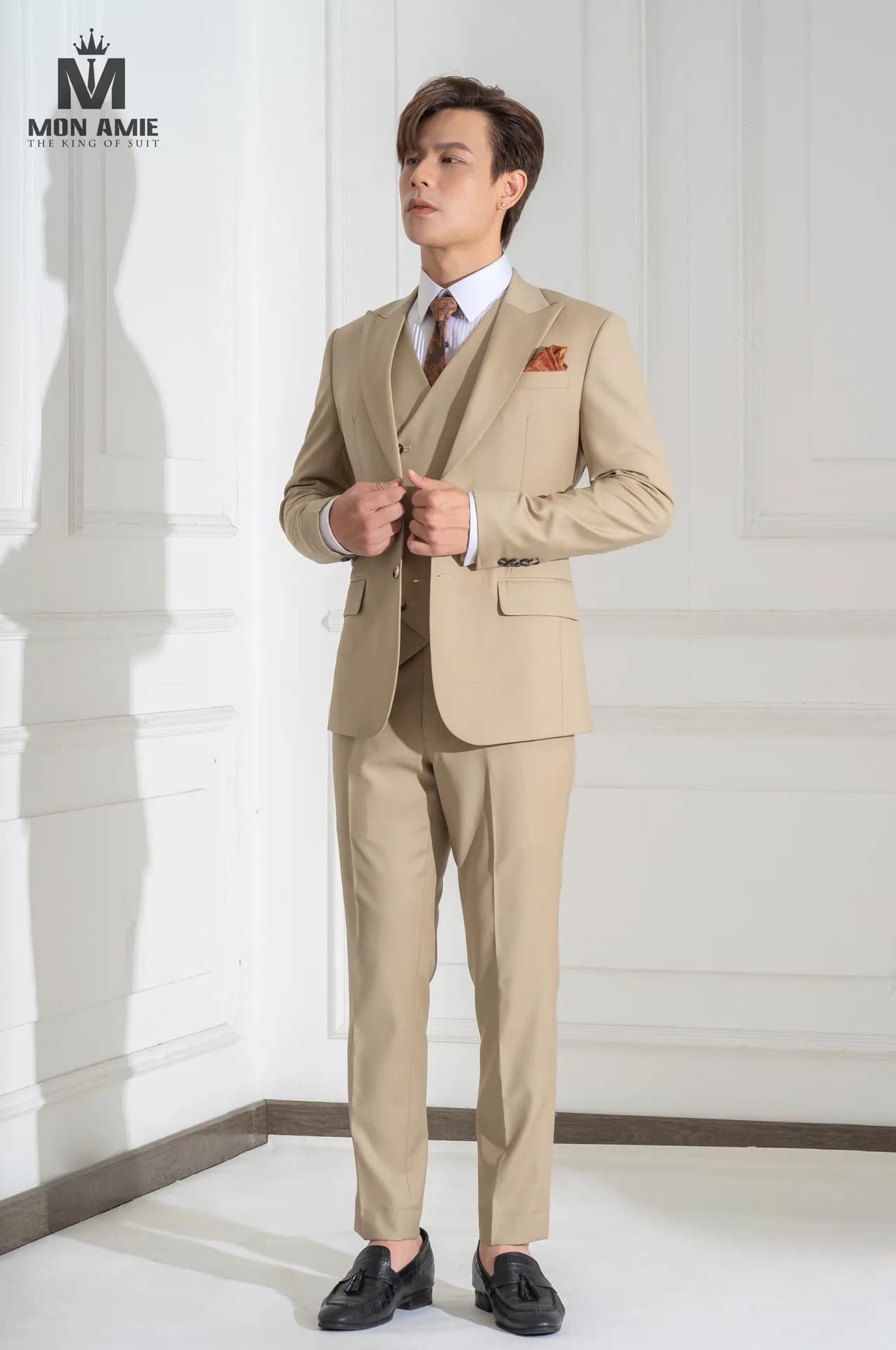 Suit ba mảnh màu be, tay cài khuy áo, dáng nghiêng trên nền studio trắng