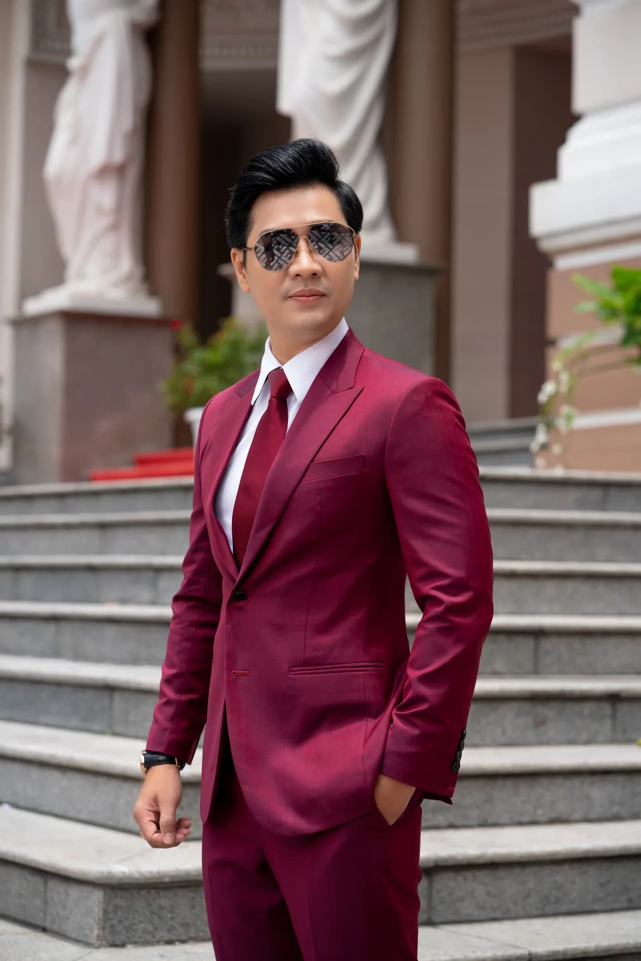 Suit đỏ rượu vang, kính phi công, đứng trên bậc thềm công trình cổ