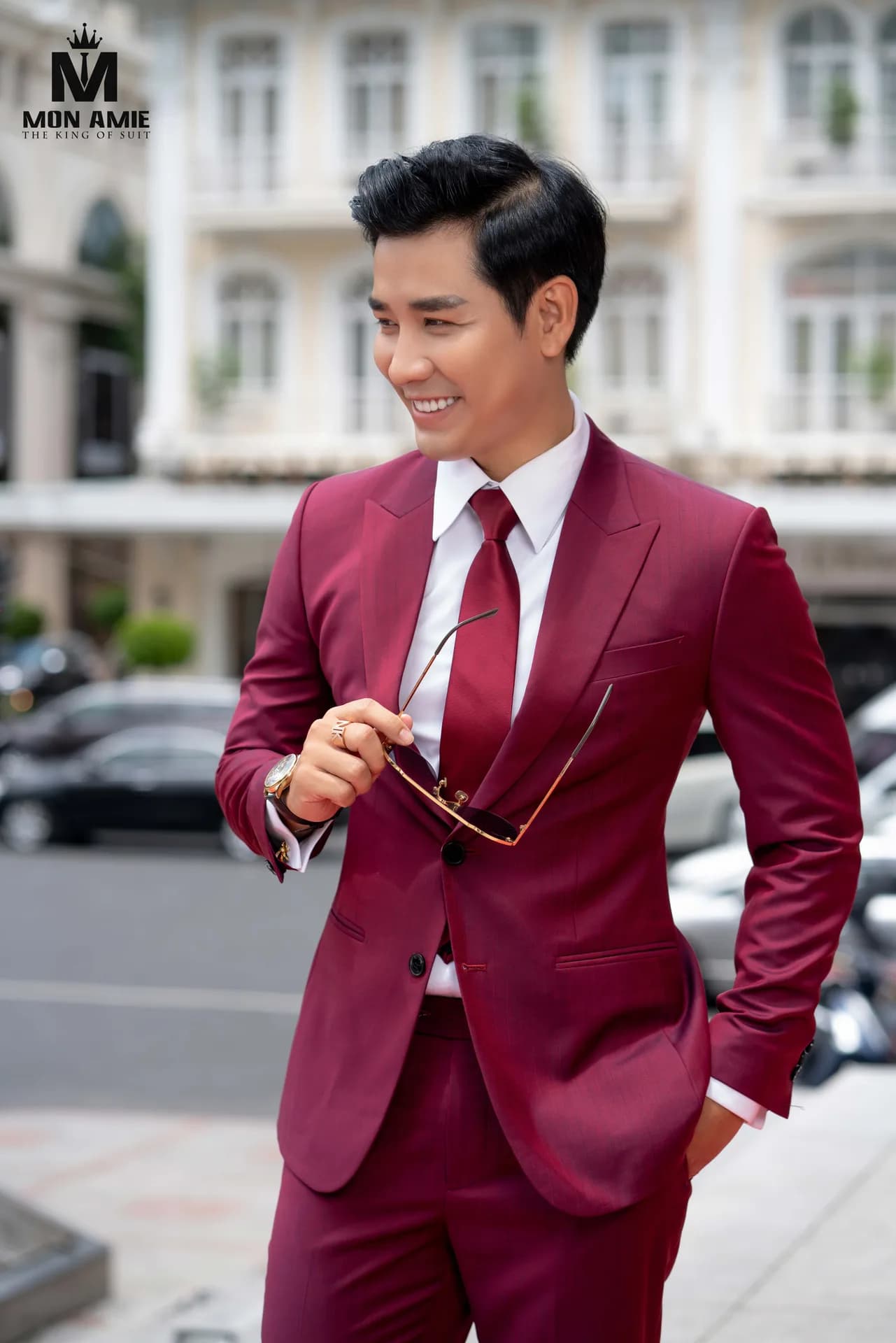Suit đỏ rượu vang, kính cầm tay, nụ cười tươi bên phố cổ