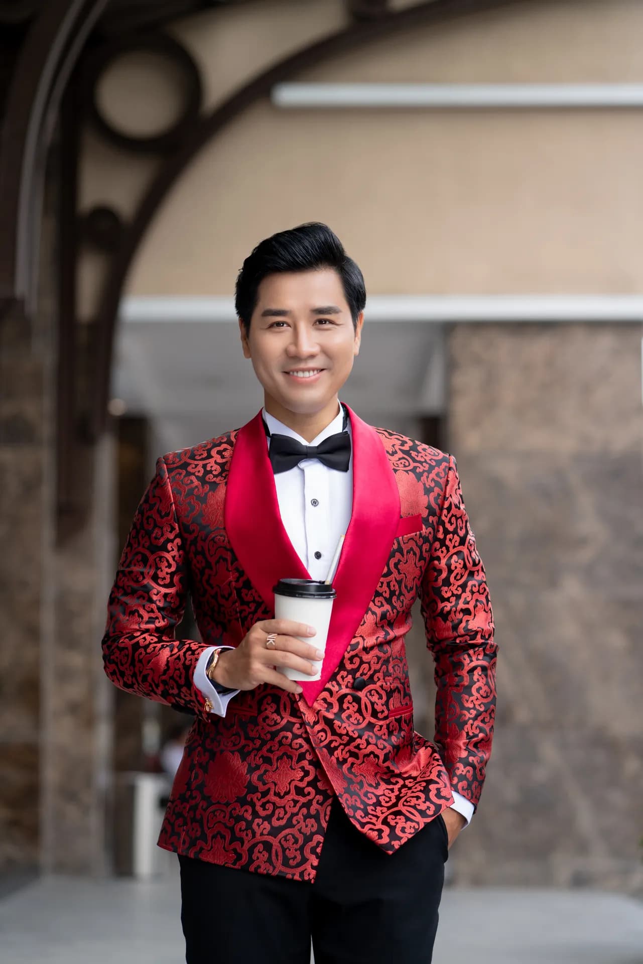 Tuxedo họa tiết đỏ ve nhung, nơ đen, cận cảnh trước tường đá