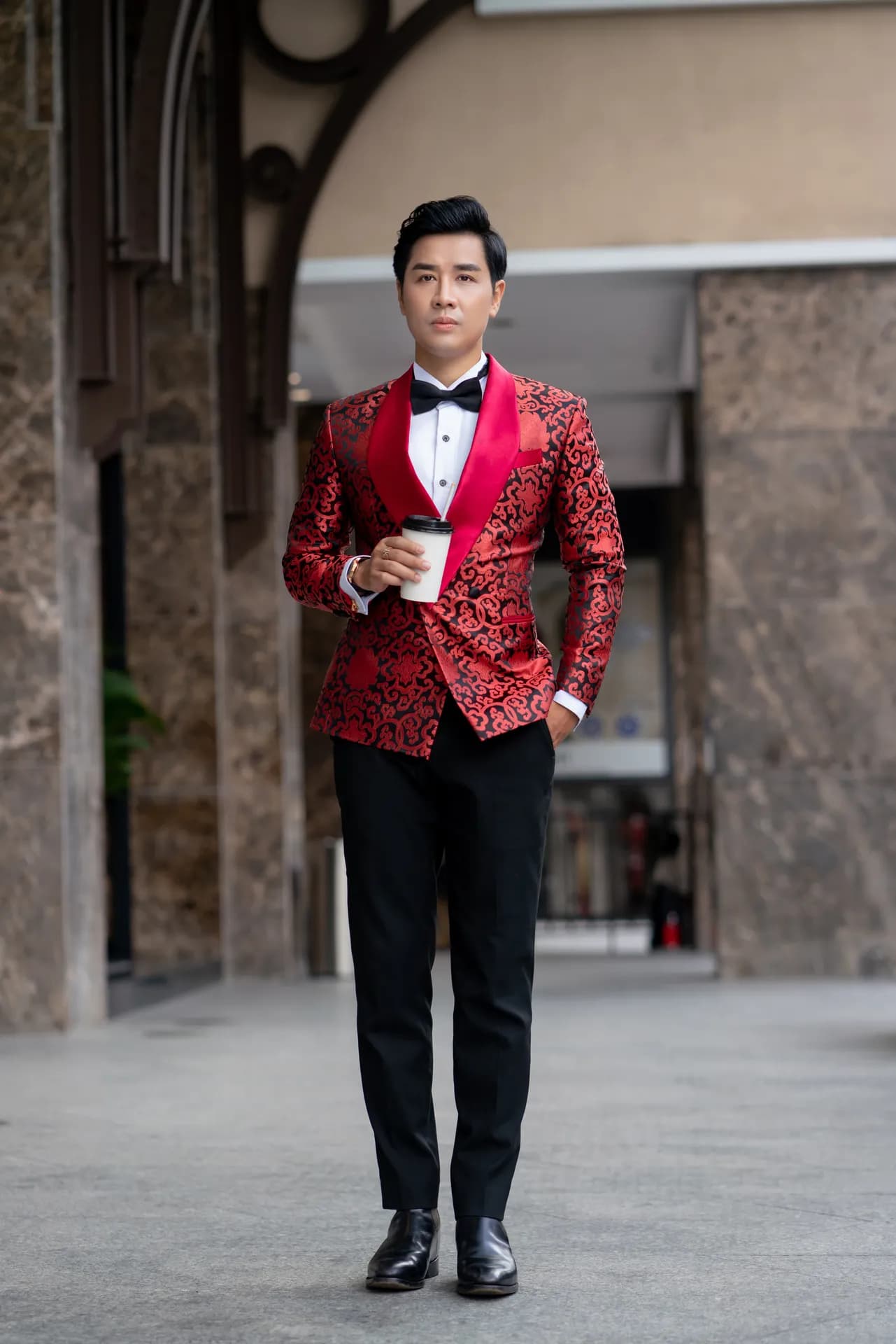 Tuxedo họa tiết đỏ, quần đen, cầm ly cà phê, đứng toàn thân