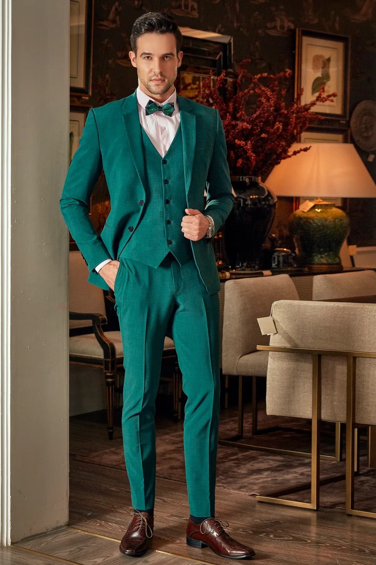 Suit ba mảnh xanh ngọc lục bảo, nơ cùng tông, đứng bên cửa phòng ăn