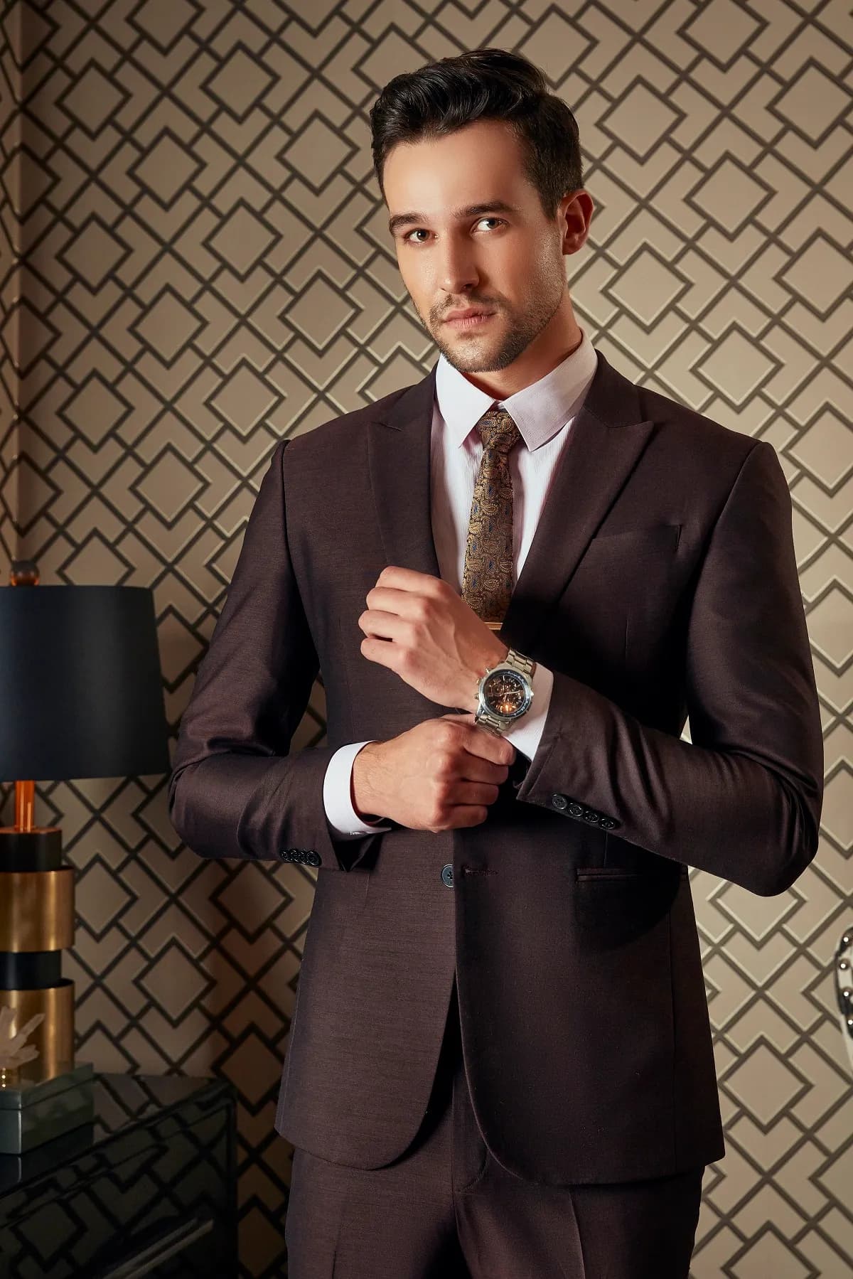 Suit nâu socola, cà vạt họa tiết, chỉnh đồng hồ trong phòng hoa văn hình học
