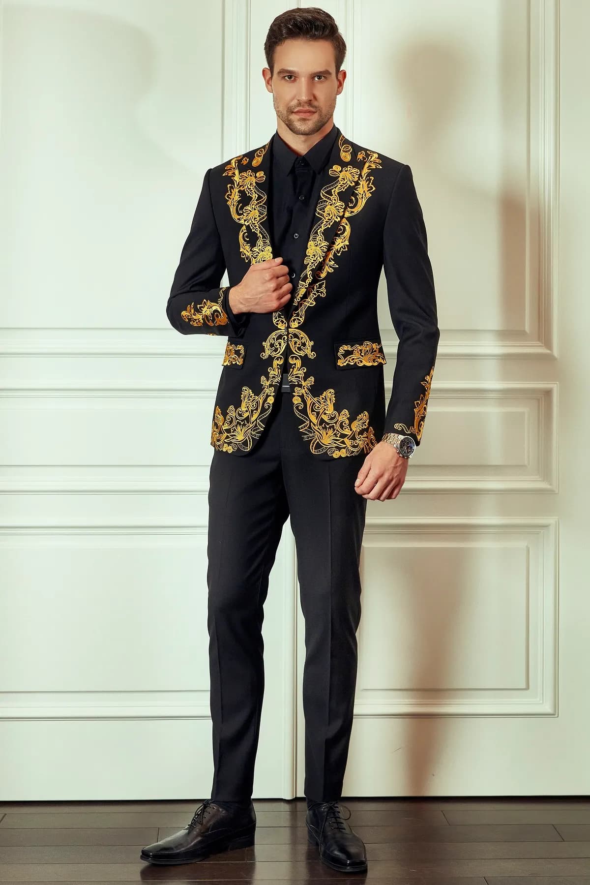 Blazer đen thêu vàng kim họa tiết thước dây, đứng trước tường trắng cổ điển