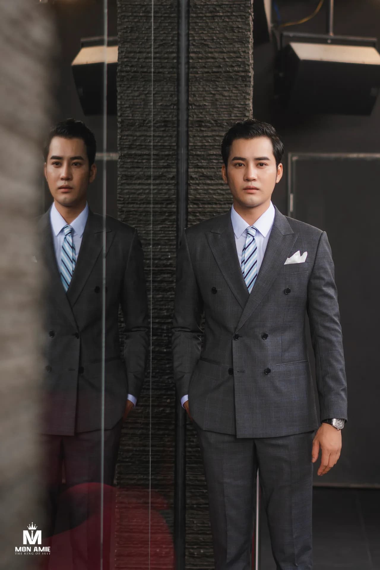 Bộ suit nâu ngồi ghế mây, sàn gỗ và tường phào chỉ trắng