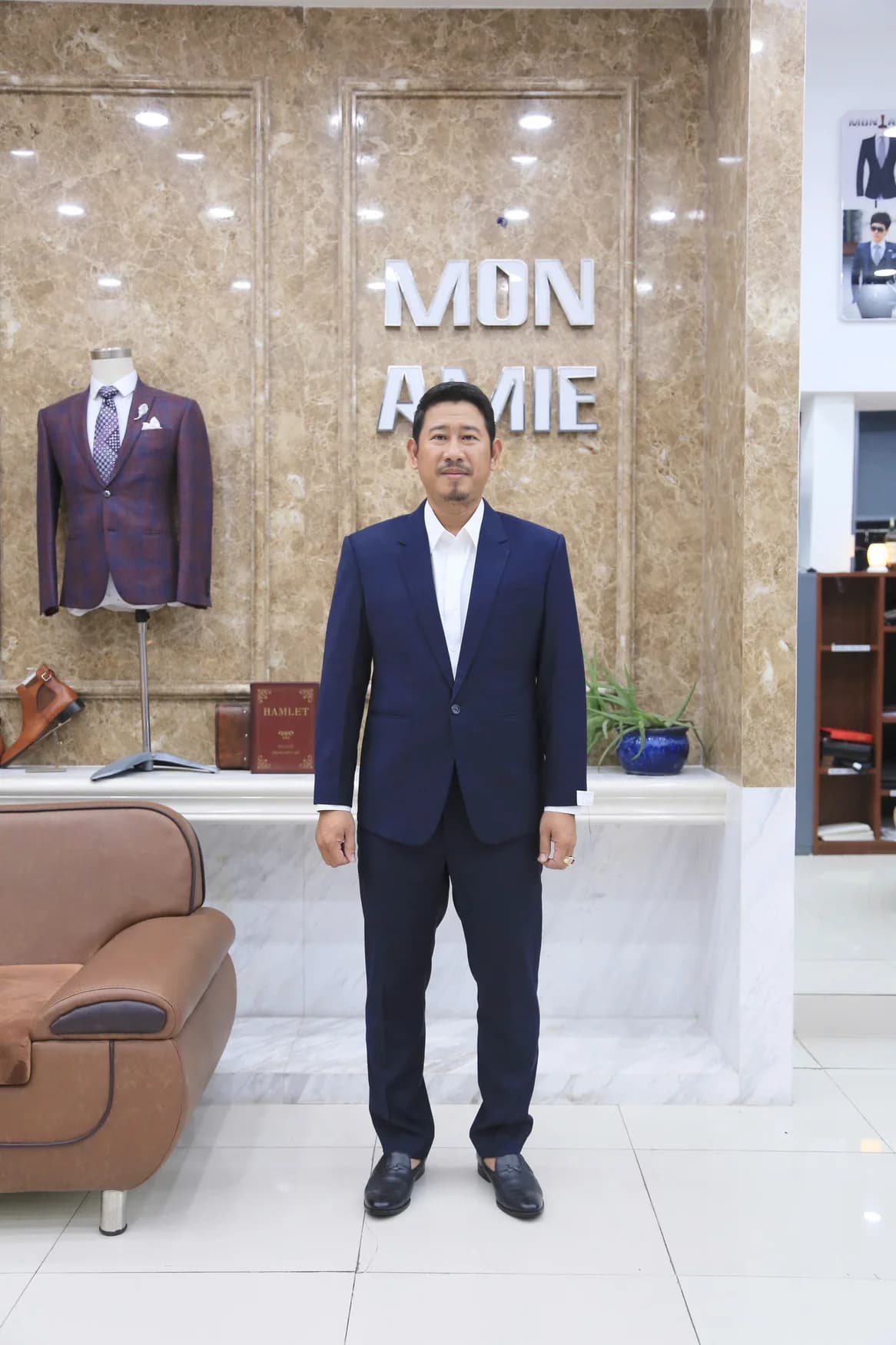 Người đàn ông vest navy, sơ mi trắng, bảng hiệu Mon Amie