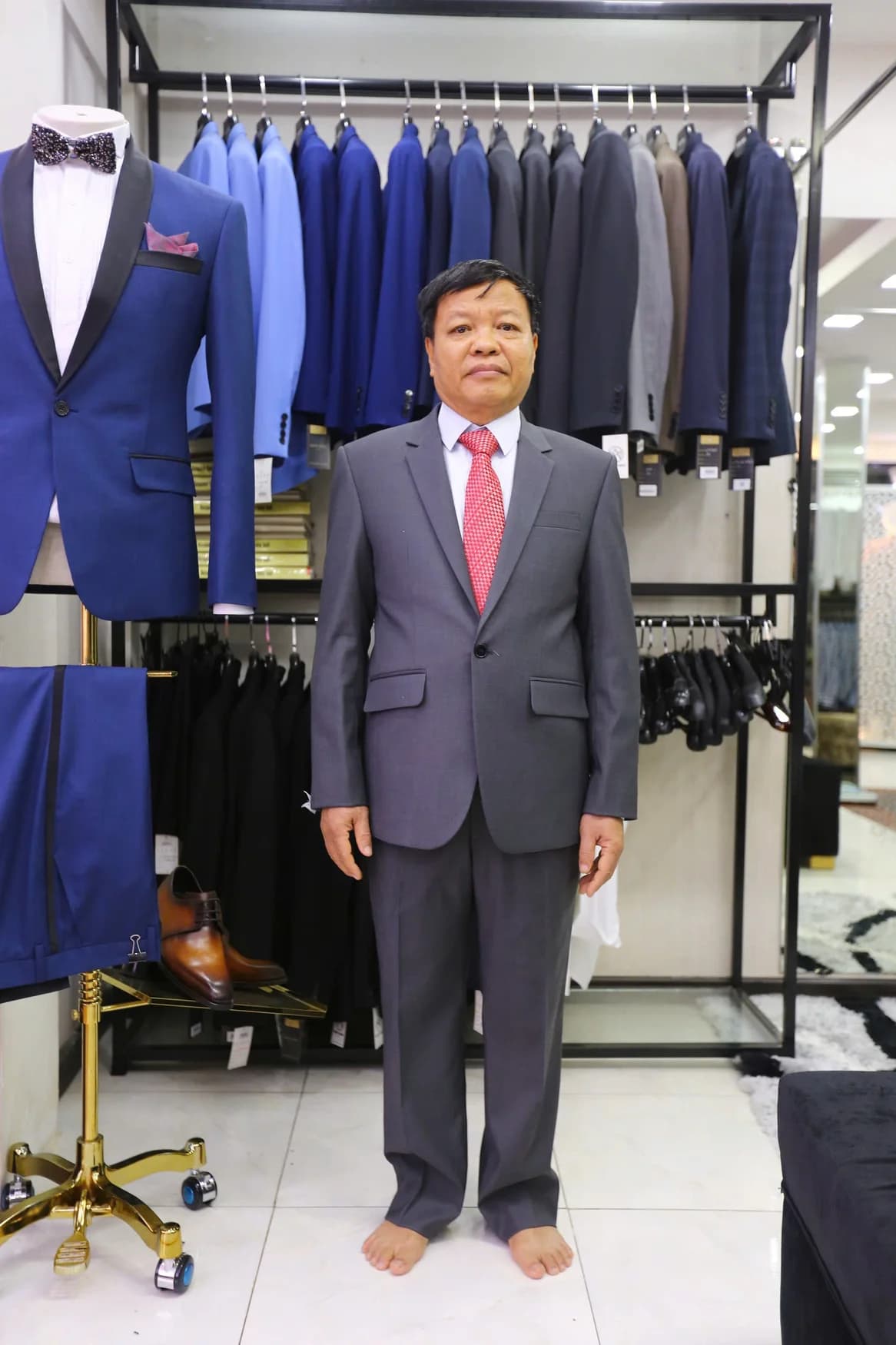 Quý ông vest xám, cà vạt đỏ hồng, đứng giữa cửa hàng