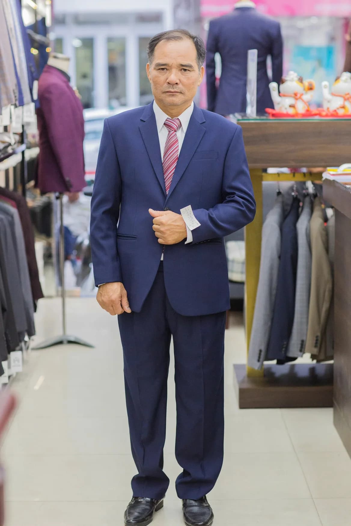 Quý ông vest navy, cà vạt sọc đỏ trắng, chỉnh nút áo
