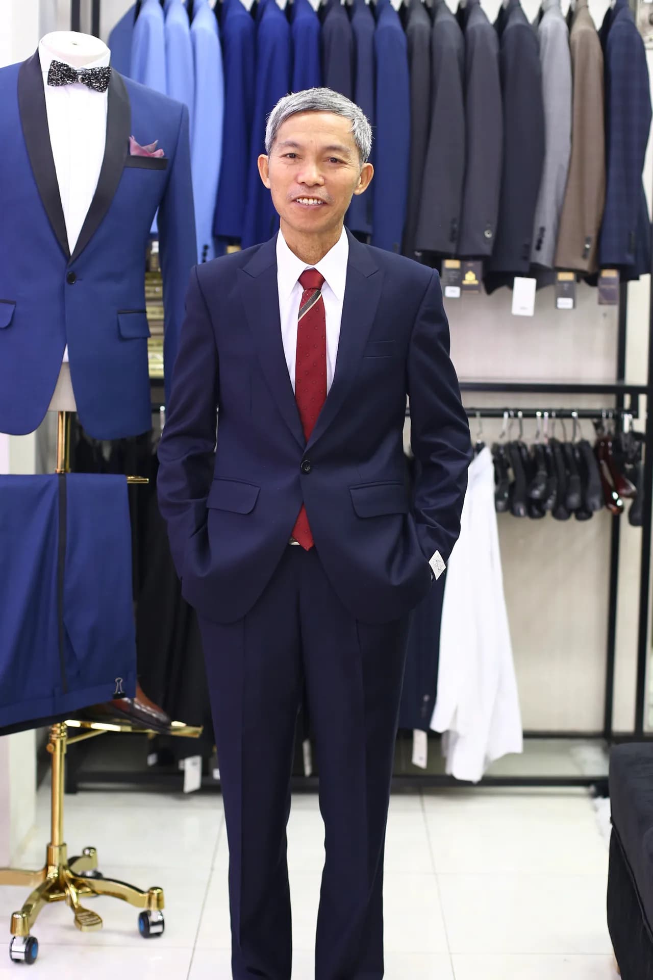 Suit navy cà vạt đỏ đô, nụ cười hài lòng bên mẫu tuxedo xanh cổ lụa