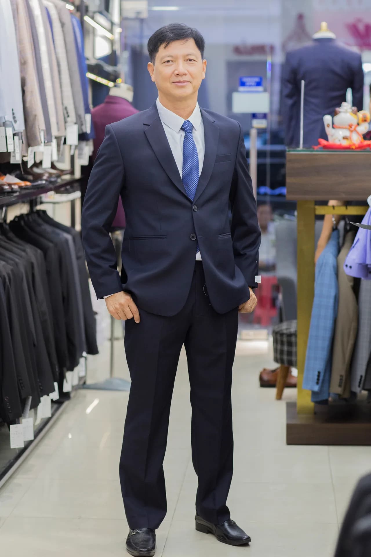 Suit navy hai cúc, cà vạt xanh chấm bi, tay đút túi, tư thế tự nhiên thoải mái