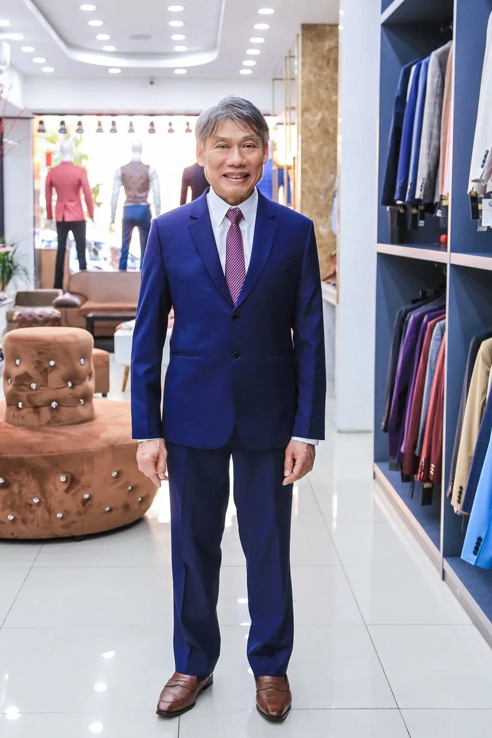 Suit xanh hoàng gia, cà vạt tím sọc, nụ cười rạng rỡ trong showroom sáng
