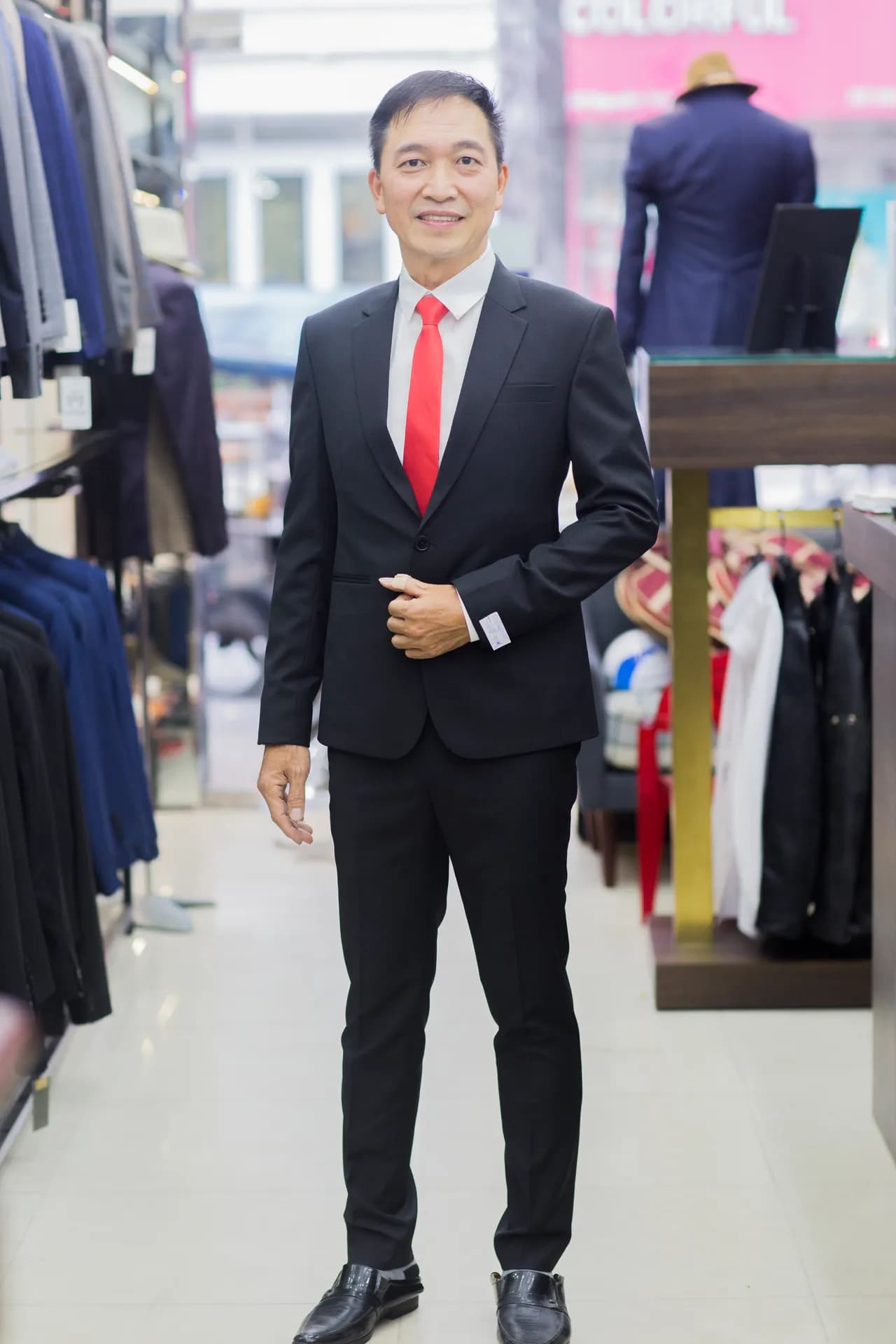 Suit đen ôm dáng, cà vạt đỏ nổi bật, nụ cười tươi tự tin