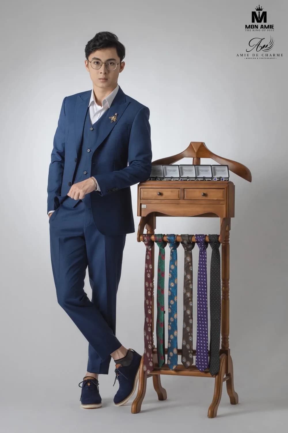 Dáng đứng tựa giá gỗ, bộ suit navy phối cà vạt nhiều họa tiết