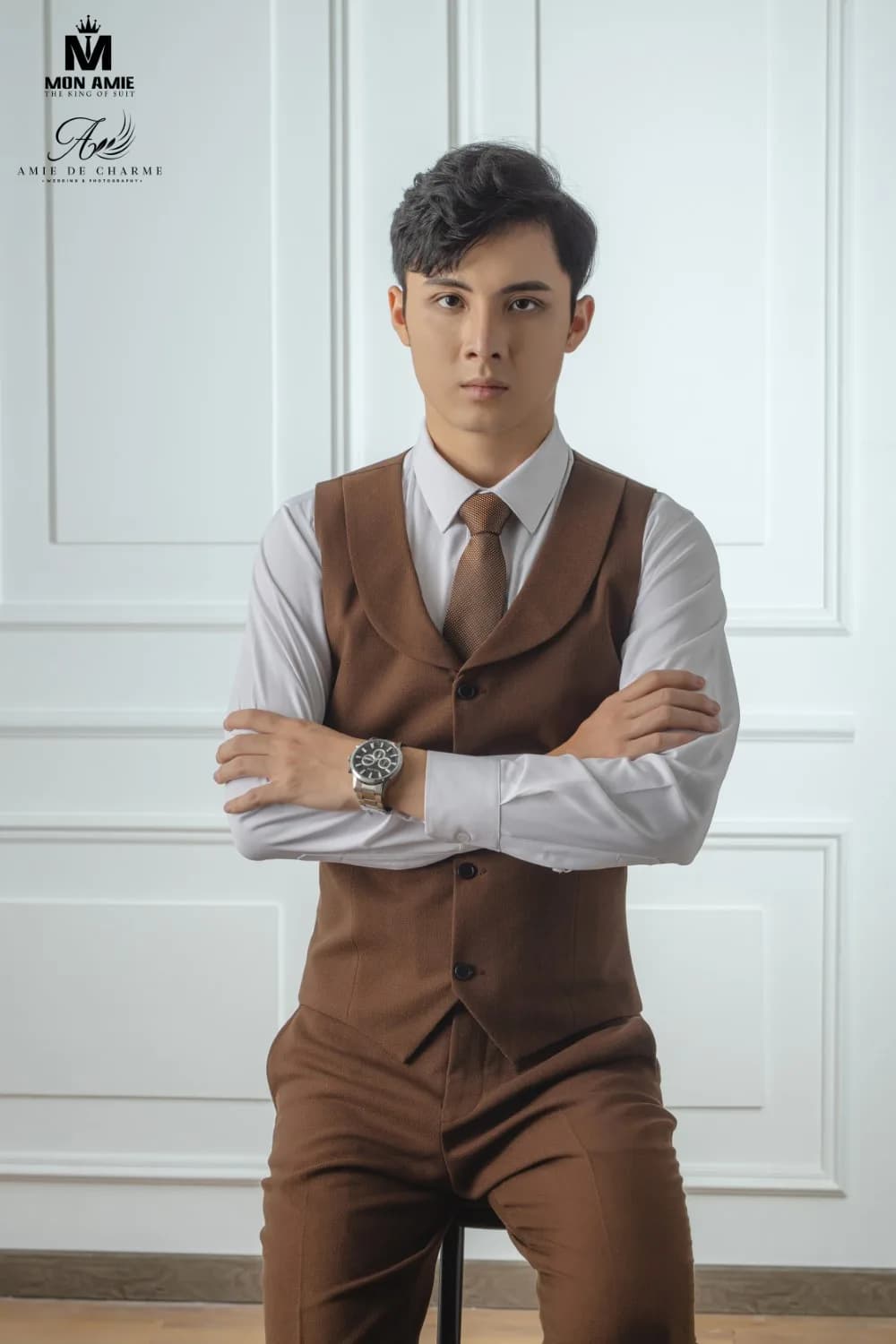 Gilê nâu cổ lá phối cà vạt cùng tông trên nền tường phào chỉ trắng