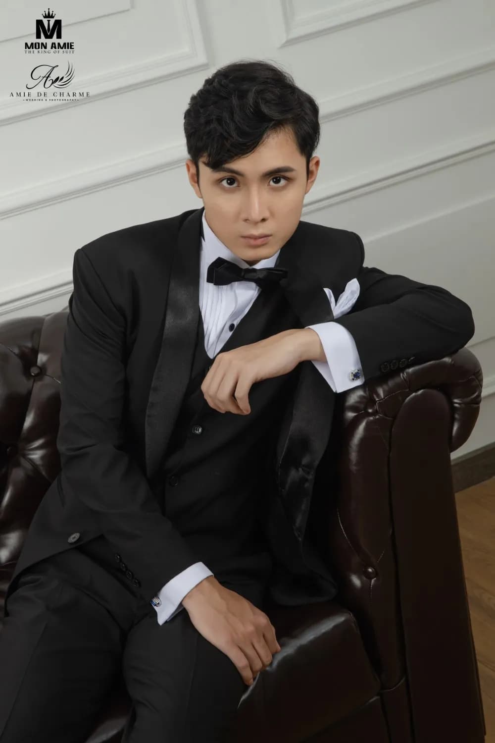 Tuxedo đen ve satin, nơ đen, tựa tay trên ghế sofa da