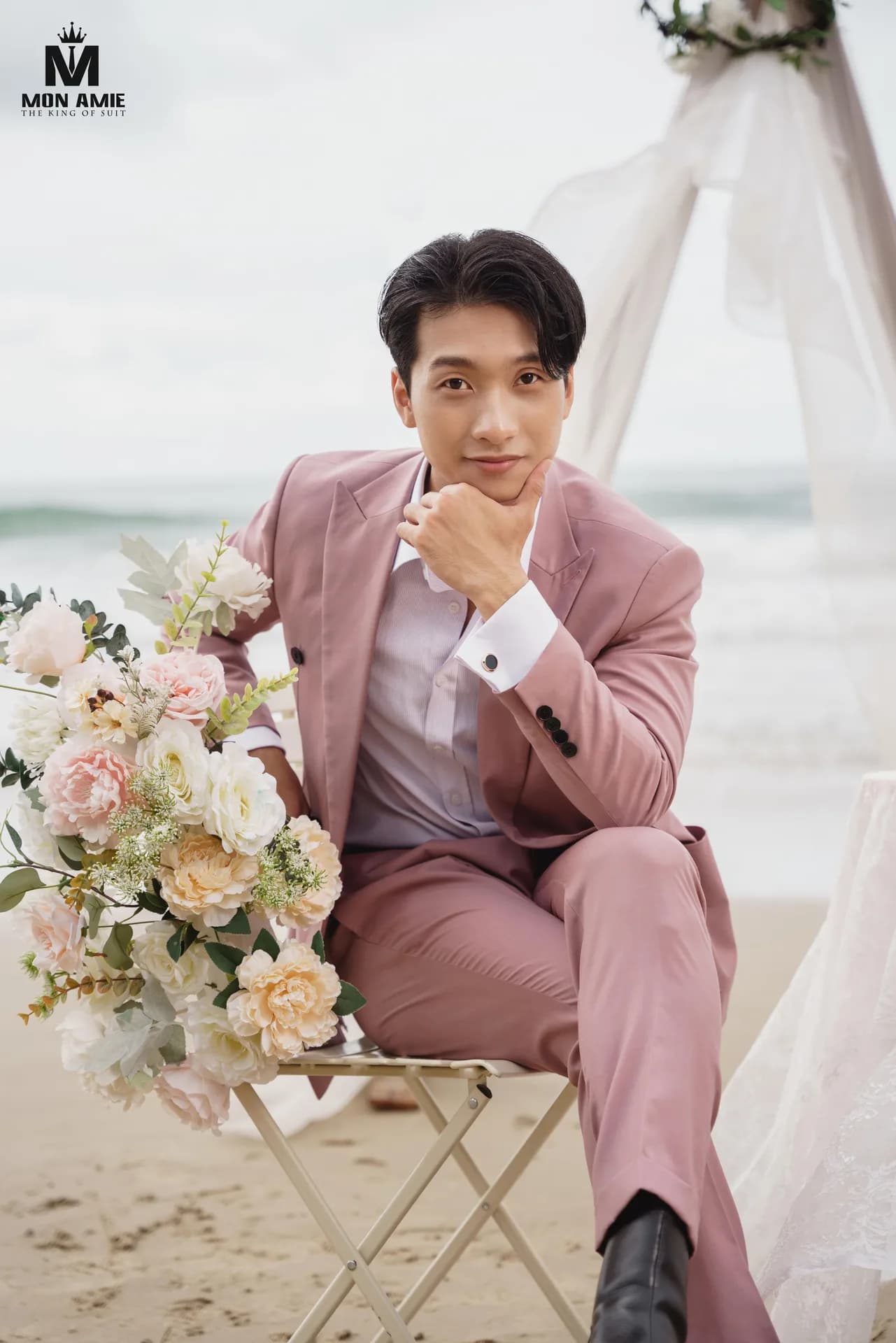 Ngồi ghế xếp cạnh bó hoa pastel, suit hồng cúc đen