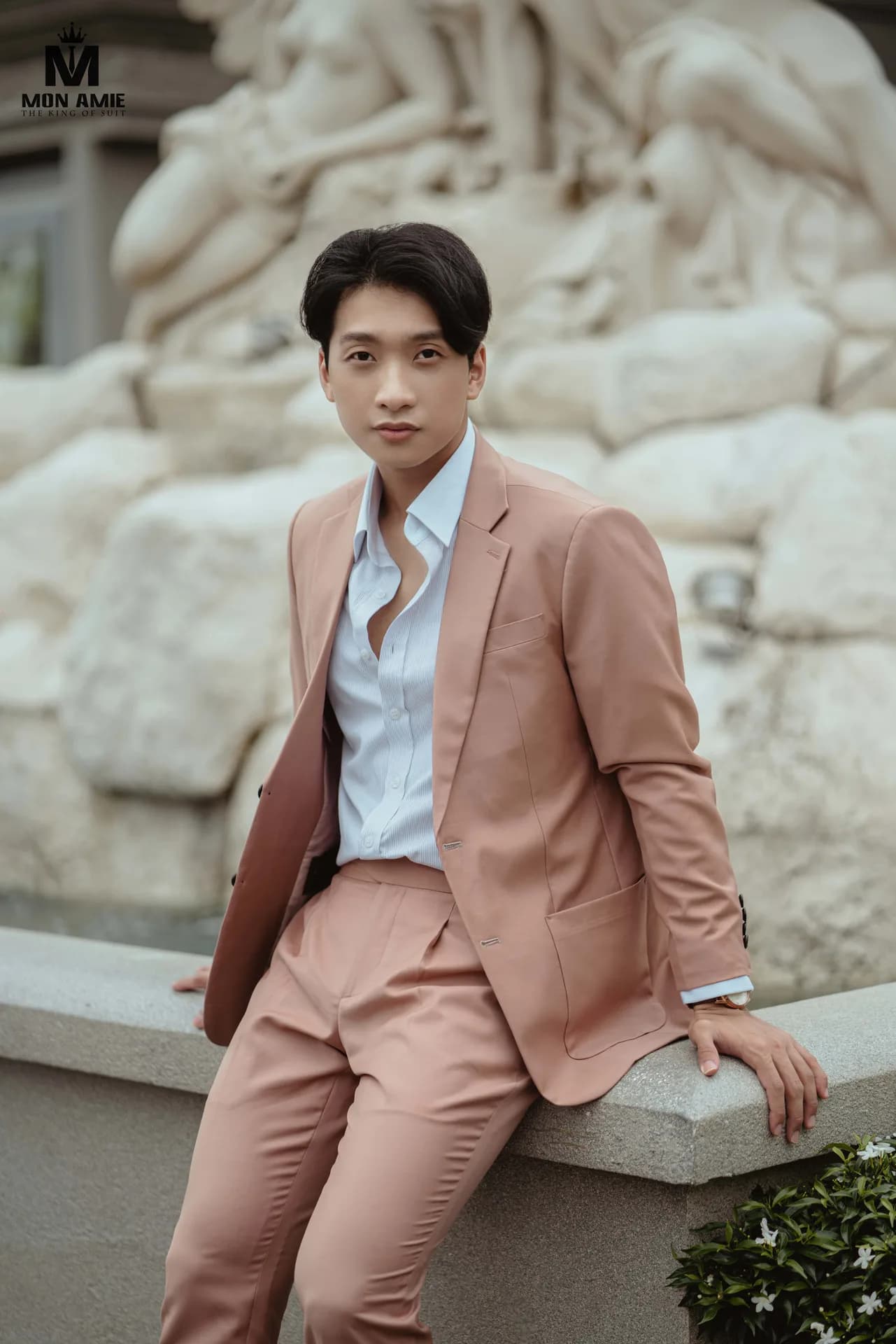 Blazer hồng đào, sơ mi trắng mở cổ tựa lan can bên phù điêu trắng