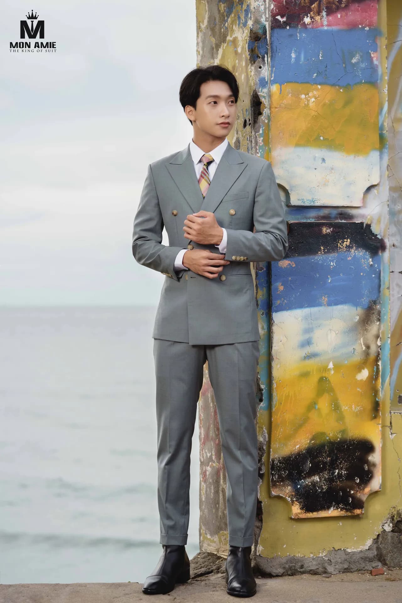 Suit xám hai hàng khuy, cà vạt caro, chỉnh măng sét bên cột tường vẽ graffiti và biển