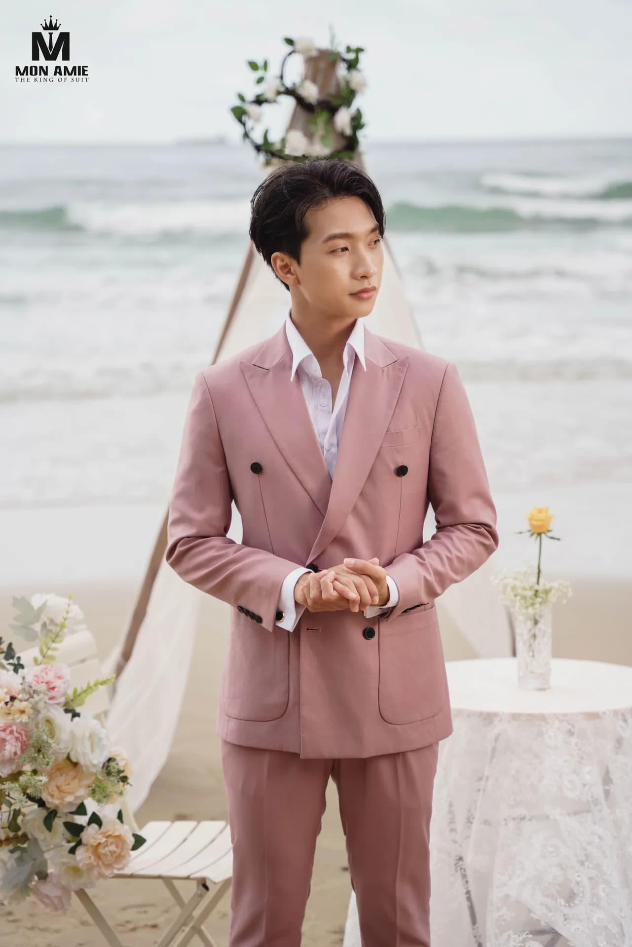 Suit hồng phấn hai hàng khuy, đứng cạnh bó hoa trên bãi biển