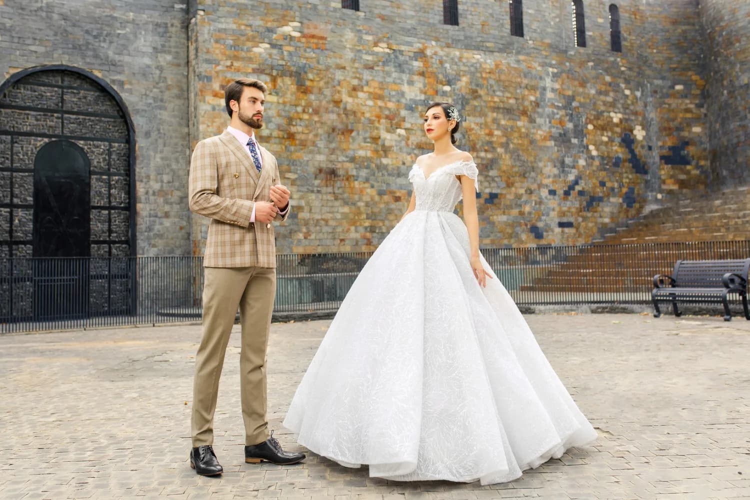 Suit caro be toàn thân bên cạnh váy cưới xòe trắng giữa sân đá