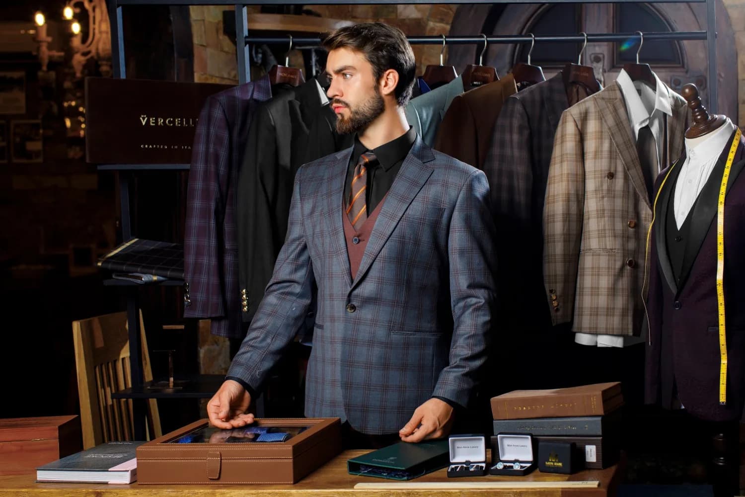 Suit caro xanh xám, gilê nâu đỏ và cà vạt sọc, đứng cạnh quầy vải