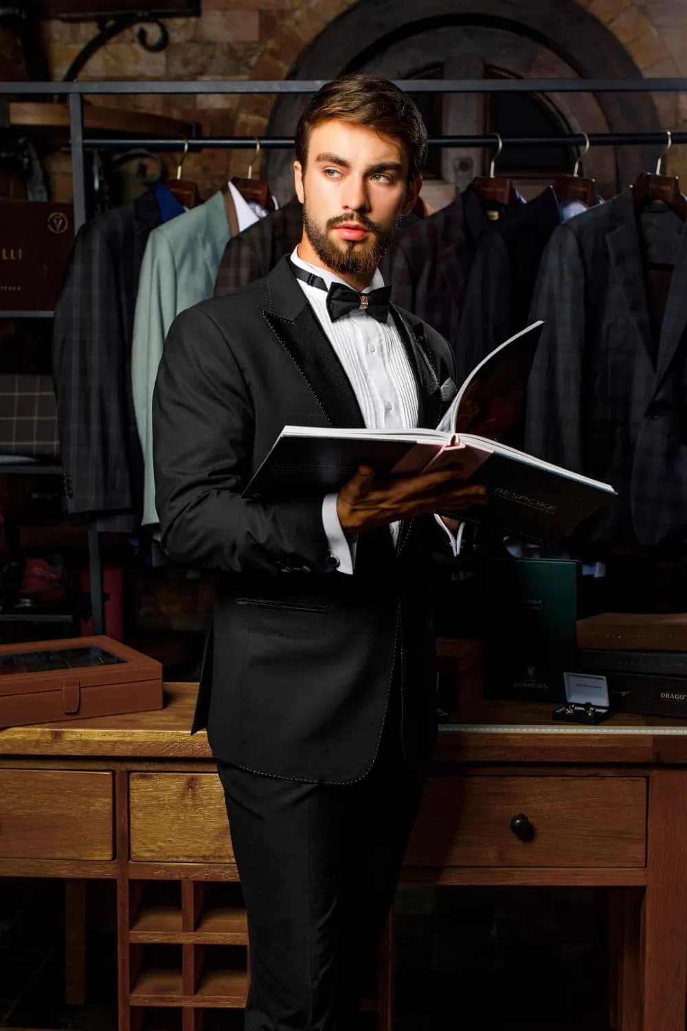 Tuxedo đen thắt nơ, đang lật cuốn catalogue vải trong xưởng may