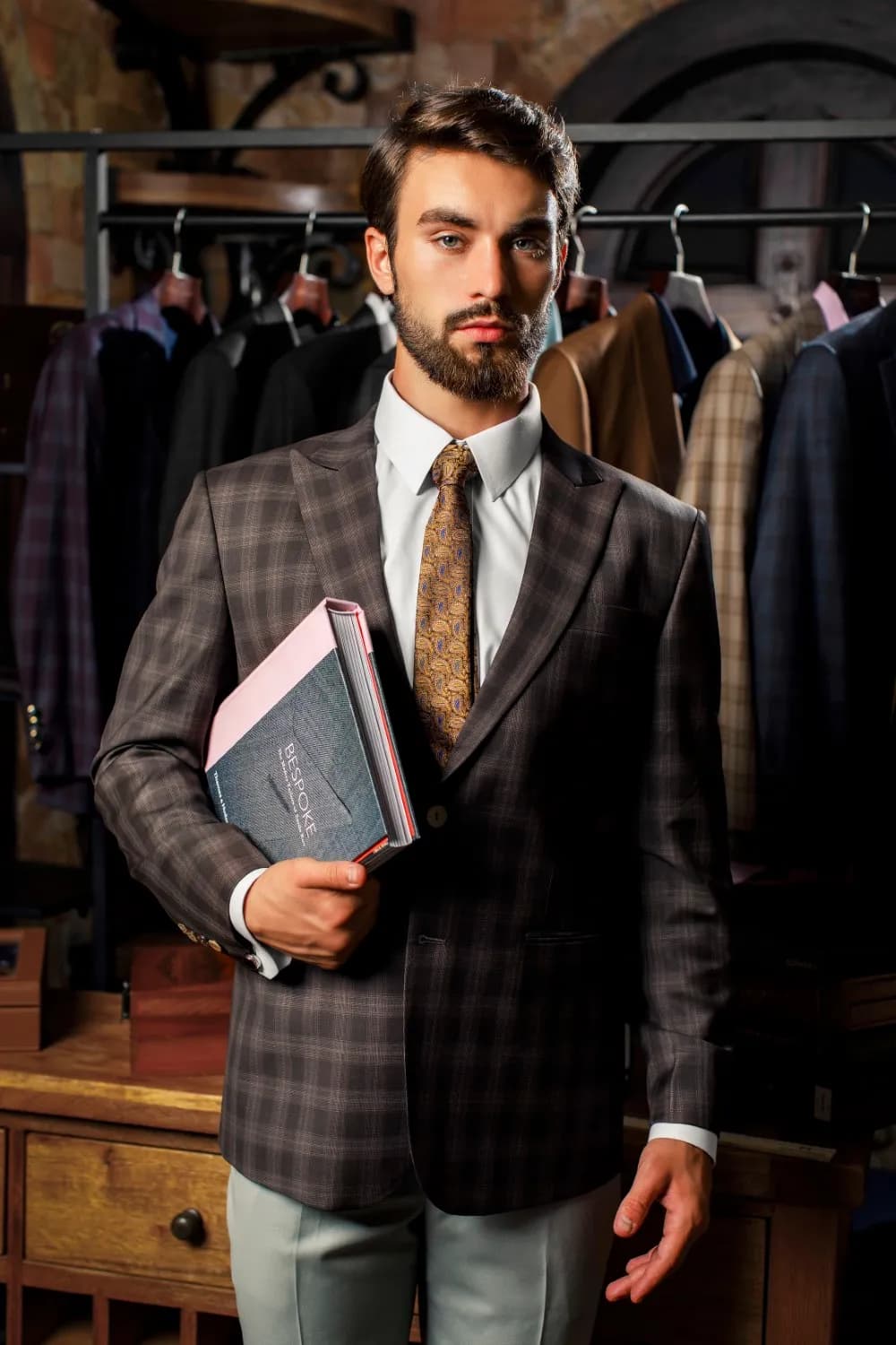 Suit kẻ ô nâu, cà vạt vàng, cầm sổ mẫu vải trong xưởng may