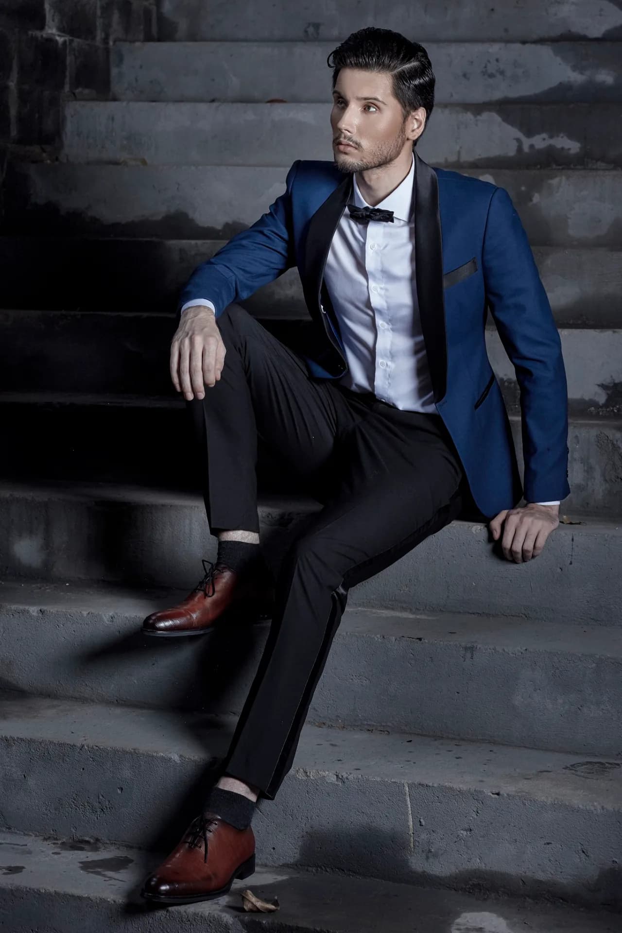 Áo tuxedo xanh coban ve đen, dáng ngồi trên bậc thang đá