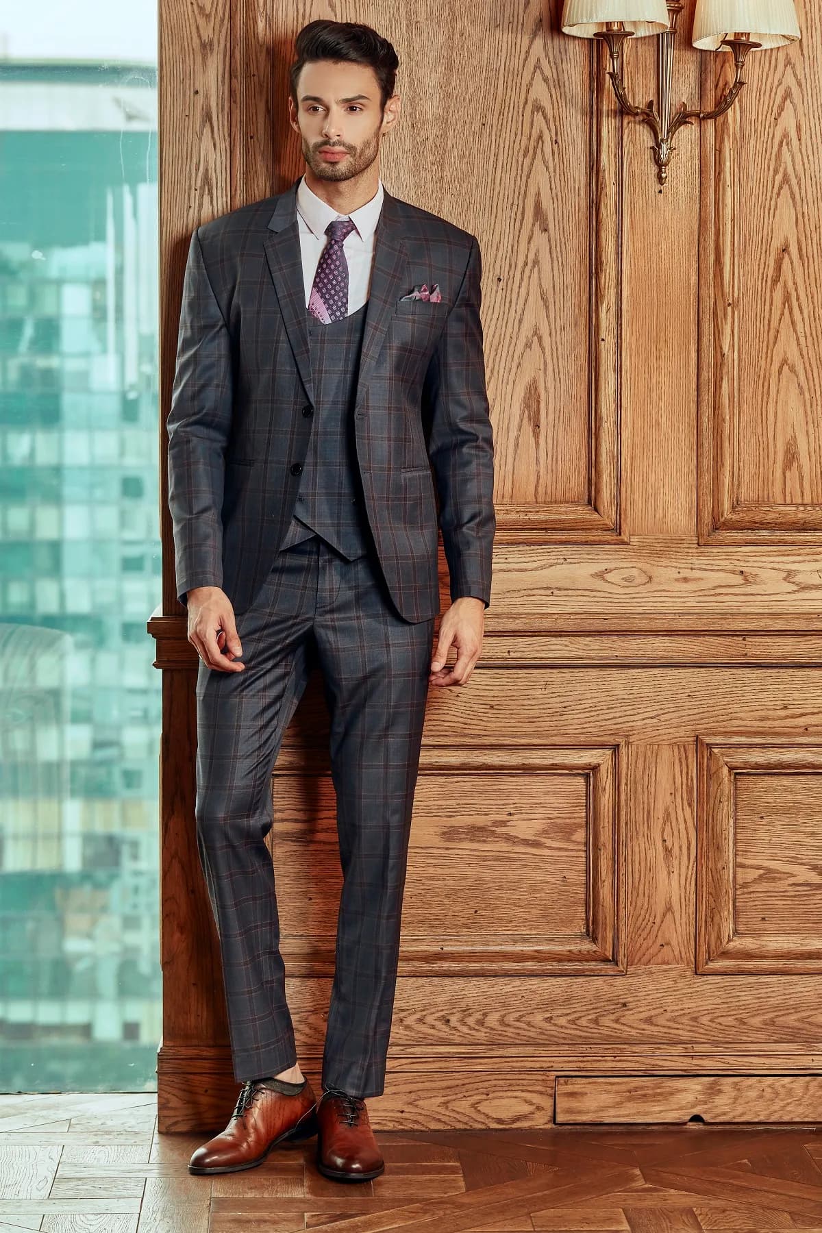 Suit ba mảnh xanh xám kẻ ô, cà vạt tím, đứng toàn thân trước tường ốp gỗ