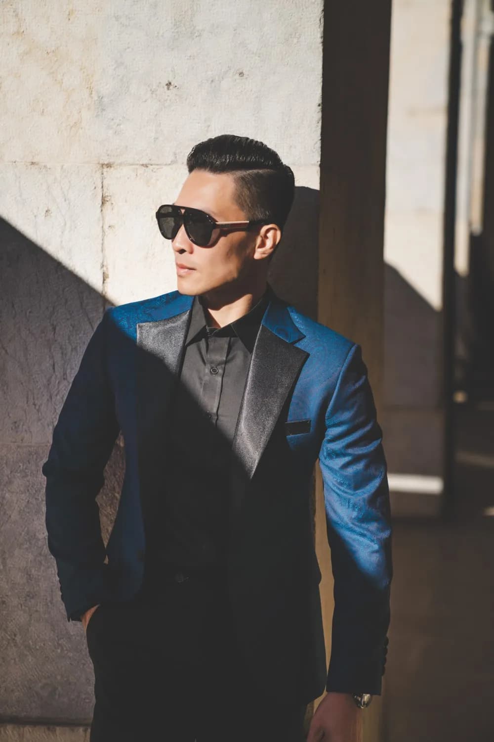 Blazer xanh paisley cổ ve lụa đen, sơ mi đen, ánh nắng và bóng đổ trên tường đá