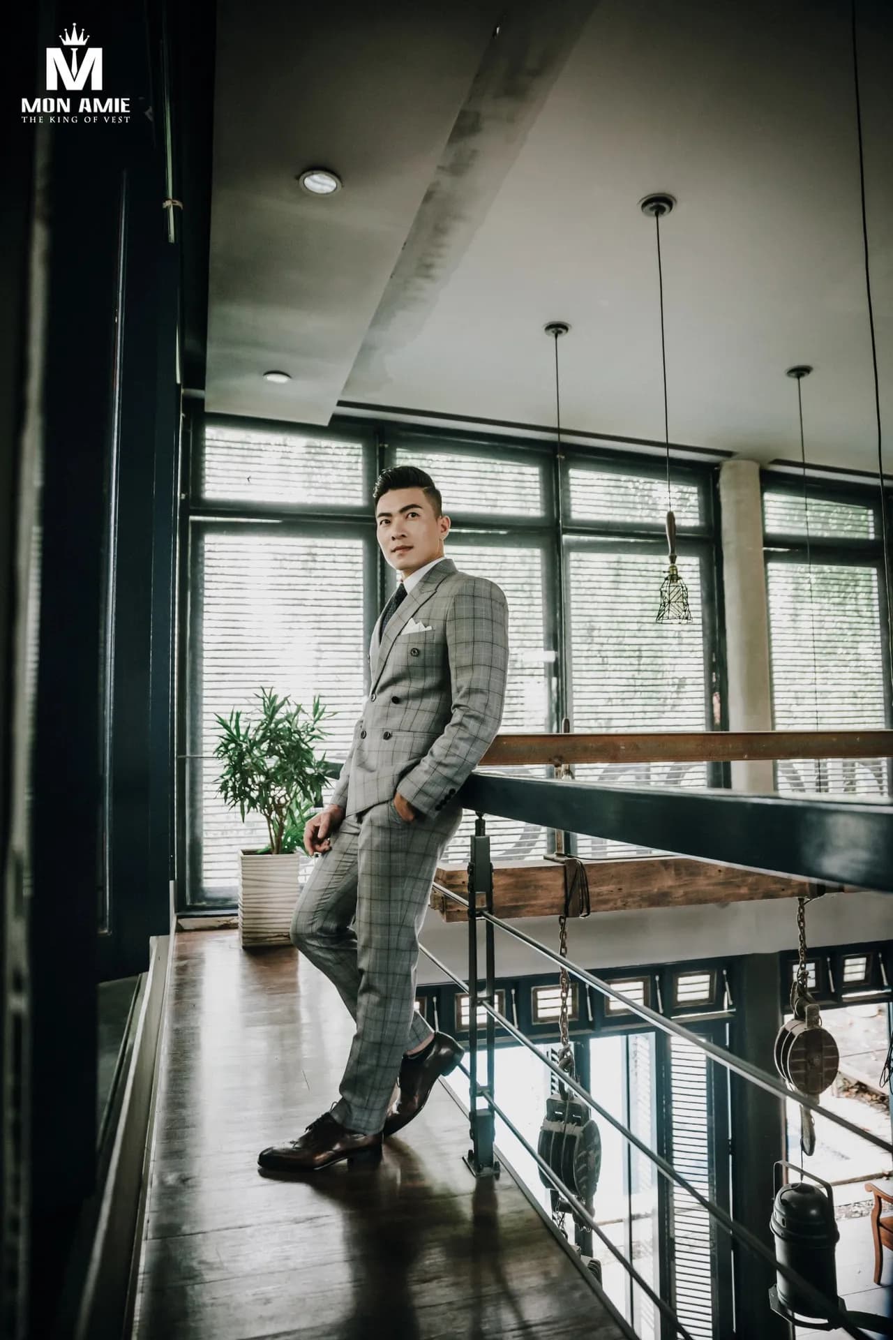 Suit caro xám hai hàng khuy, tựa lan can gác lửng, ánh sáng cửa sổ