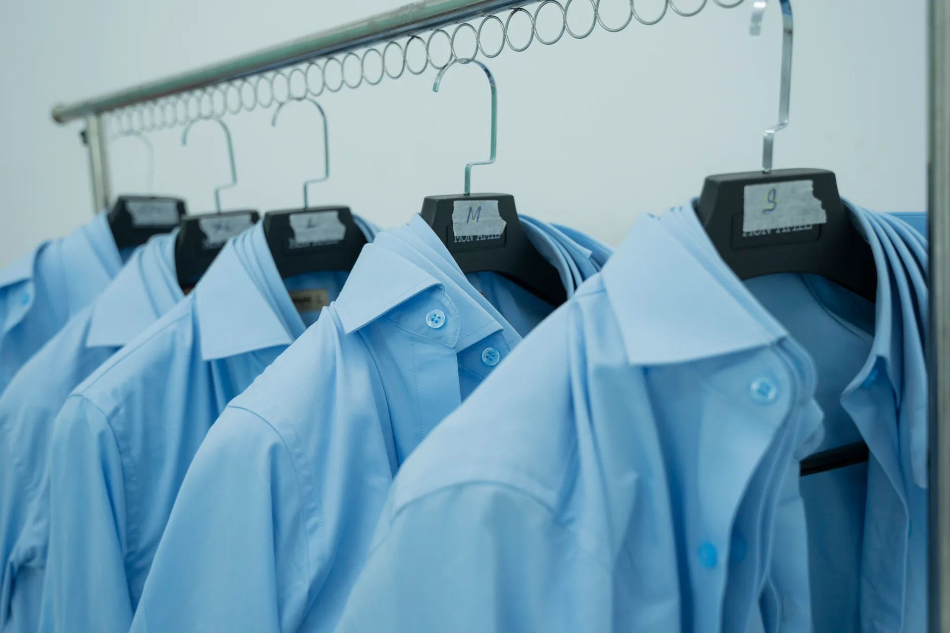 Áo sơ mi xanh mẫu gắn nhãn size S, M, L treo sẵn để nhân viên thử